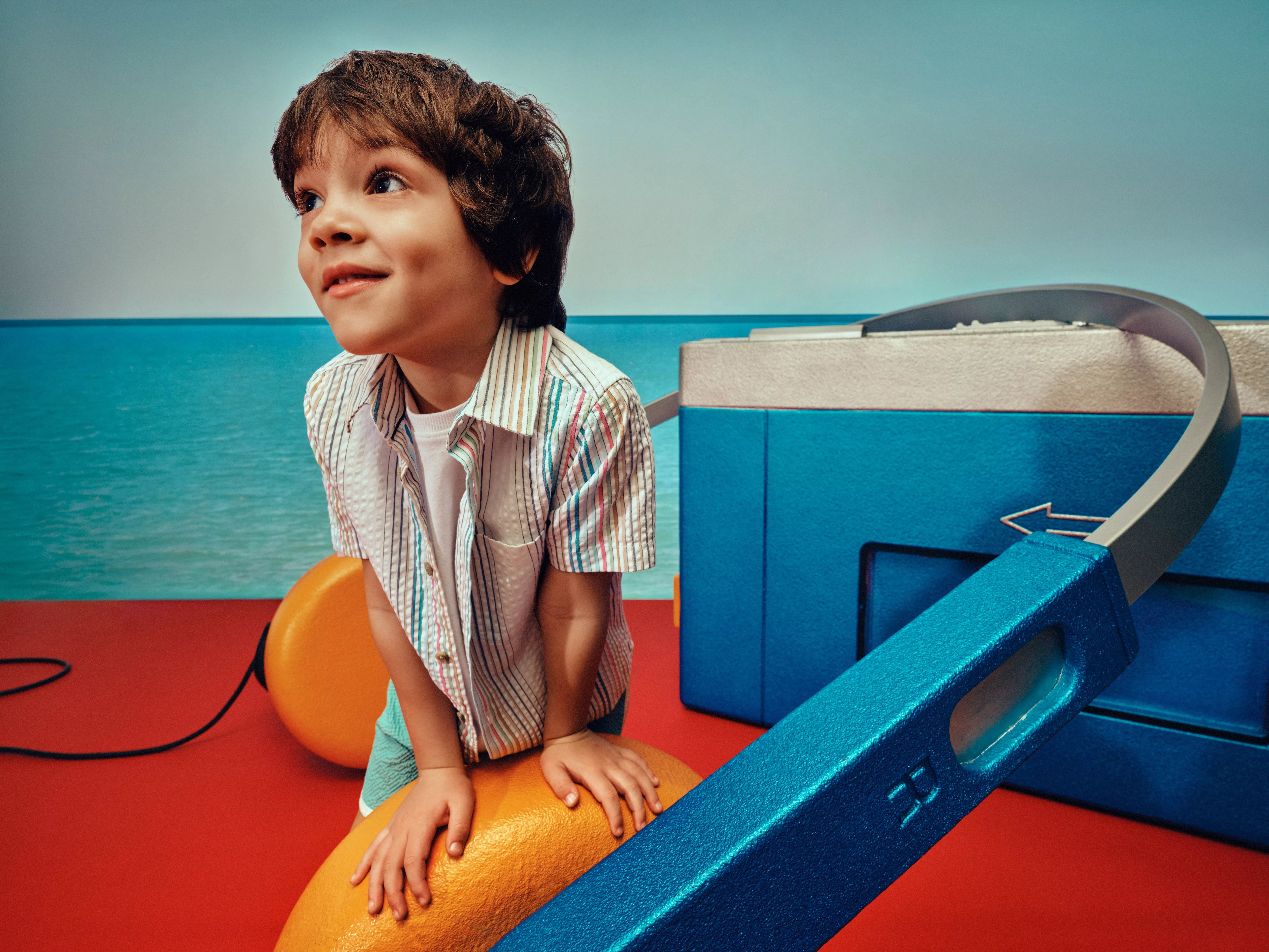 Smiling young boy playing on colourful indoor soft play equipment with blue slide and ocean-themed backdrop