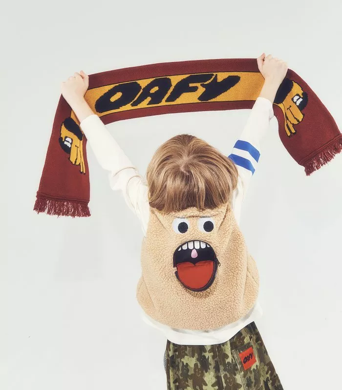 Child holding a DAFY scarf overhead, wearing a funny monster fleece vest, studio photo on white background