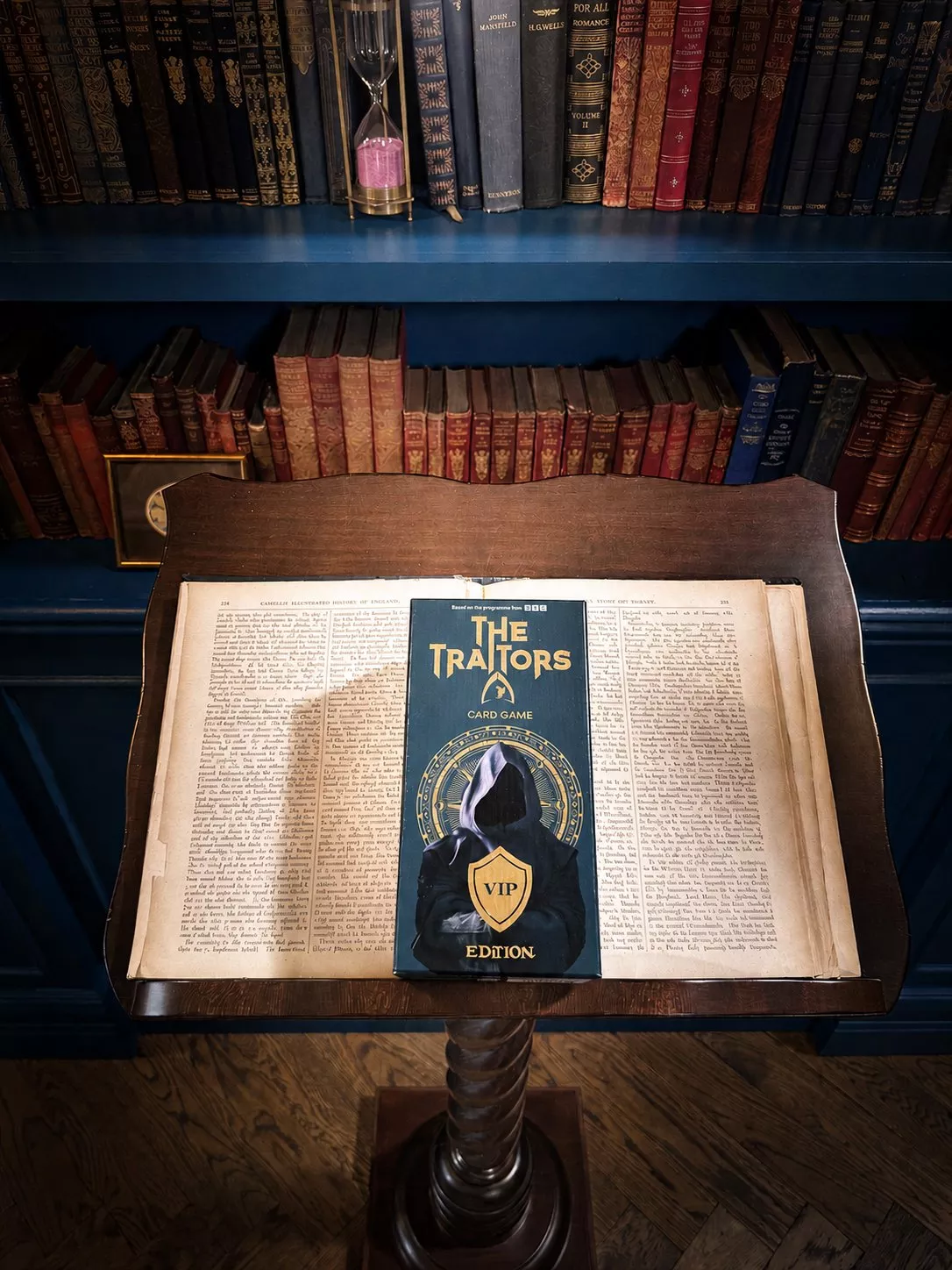 The Traitors VIP Edition card game box on an open book, set before vintage bookshelves in a cosy library.