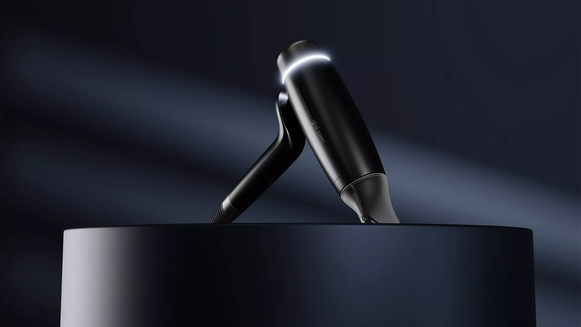 Black modern hairdryer with LED light on a dark background, angled on a pedestal, highlighting its sleek design.