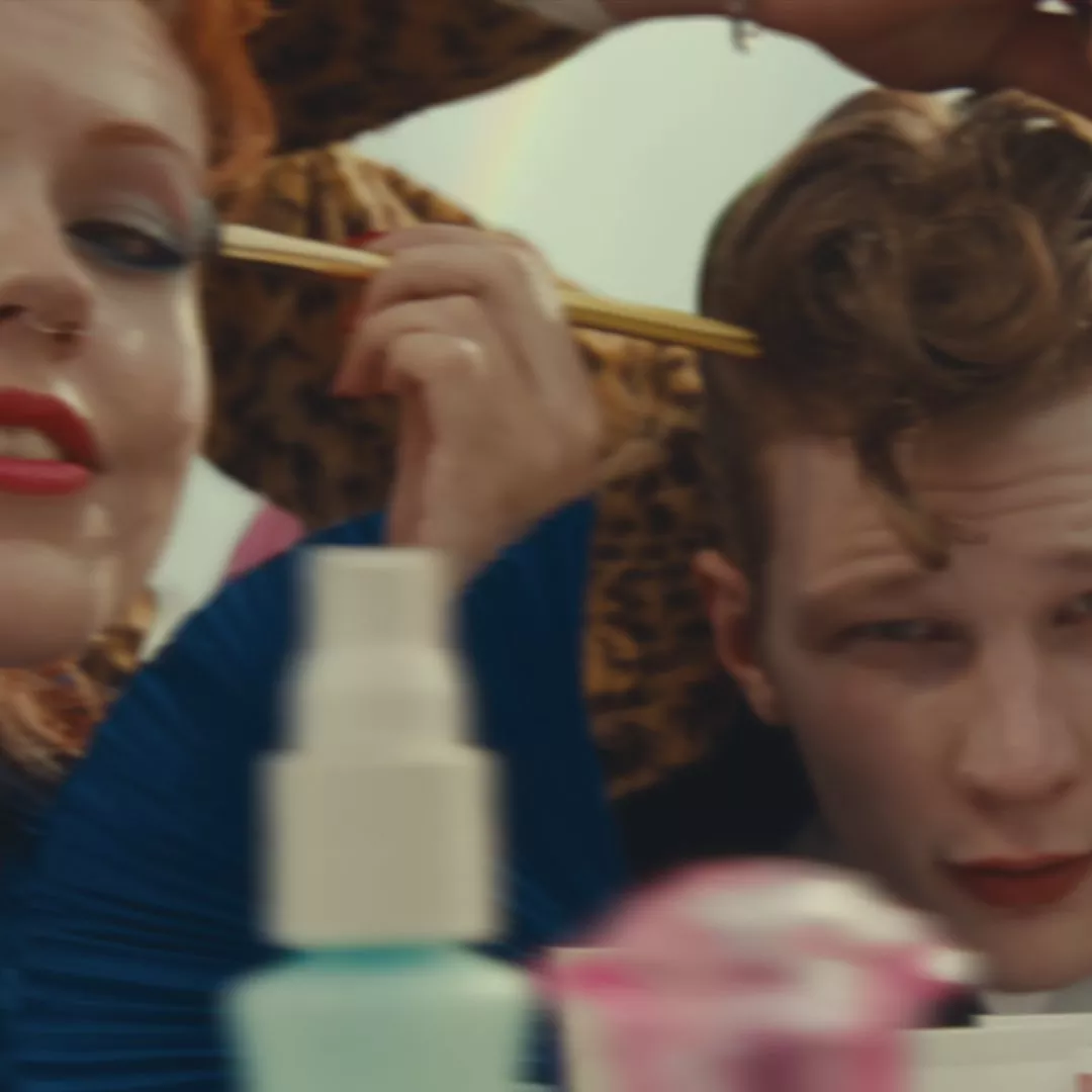 A person with vibrant makeup applies eyeliner, surrounded by beauty products and a leopard print garment.