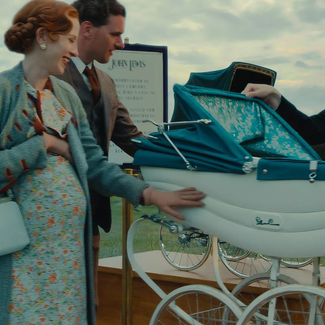 A couple admires a vintage-style pram with a blue canopy. The scene suggests a mid-20th-century setting.