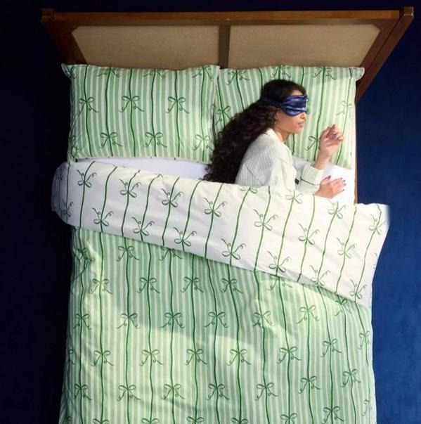 Overhead image of a person lying in a bed with an eye mask on in green and white bedding