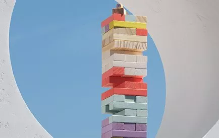 A colourful Jenga tower stands tall against a clear blue sky, framed by a circular white structure.