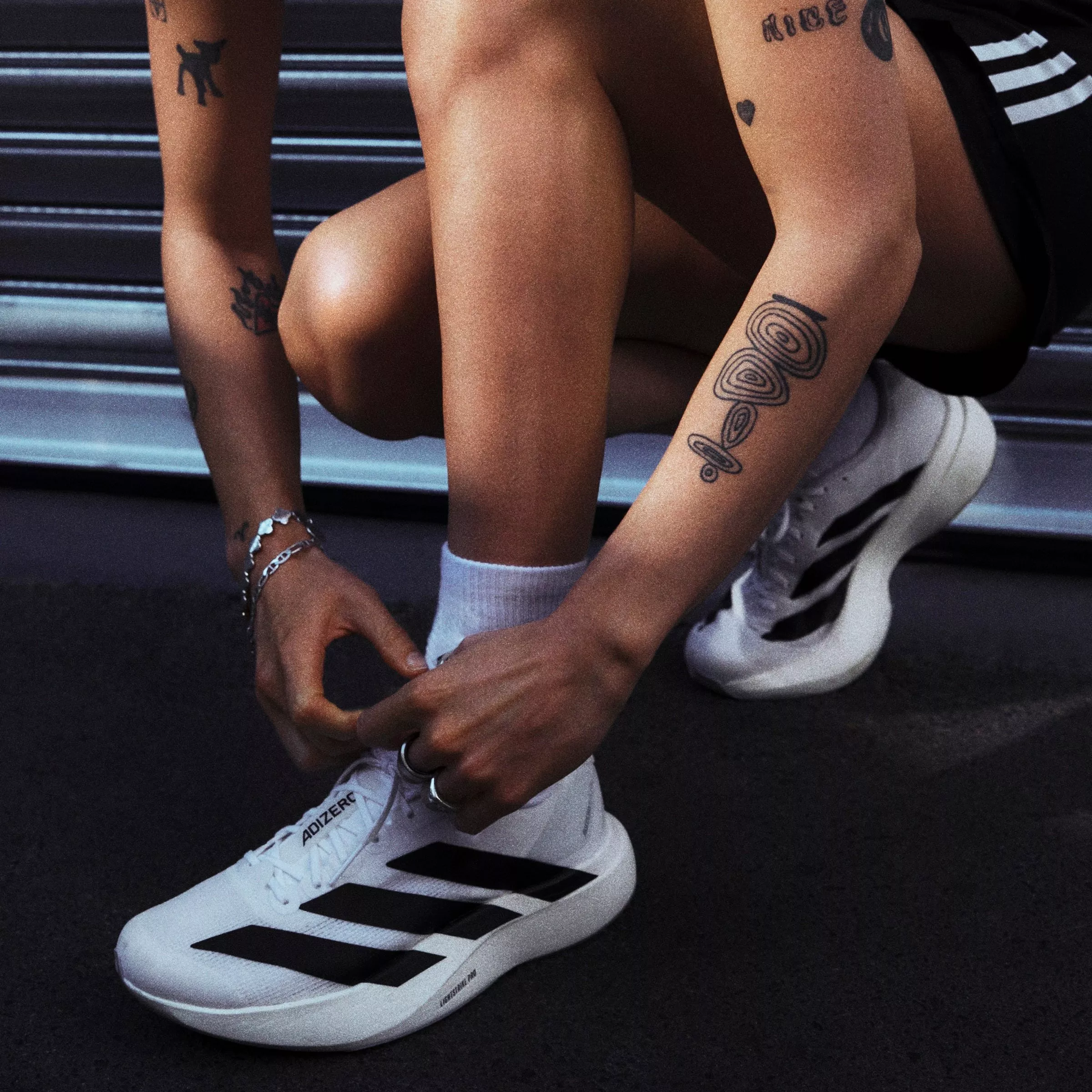 Athlete tying white Adidas Adizero running shoes on track, close-up of legs and tattooed arms pre-race