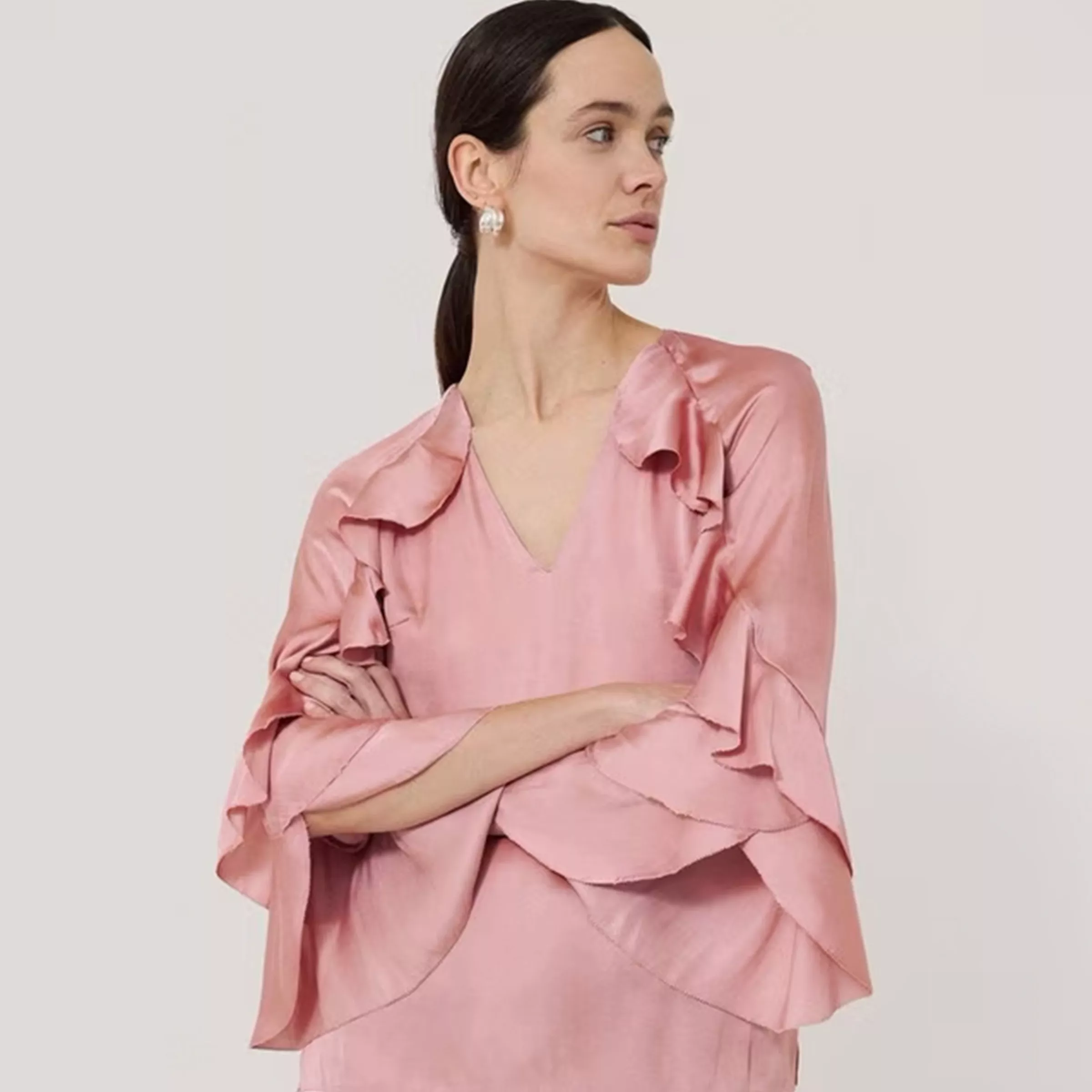 Woman modelling a blush pink satin ruffle sleeve dress, studio fashion portrait on a neutral background