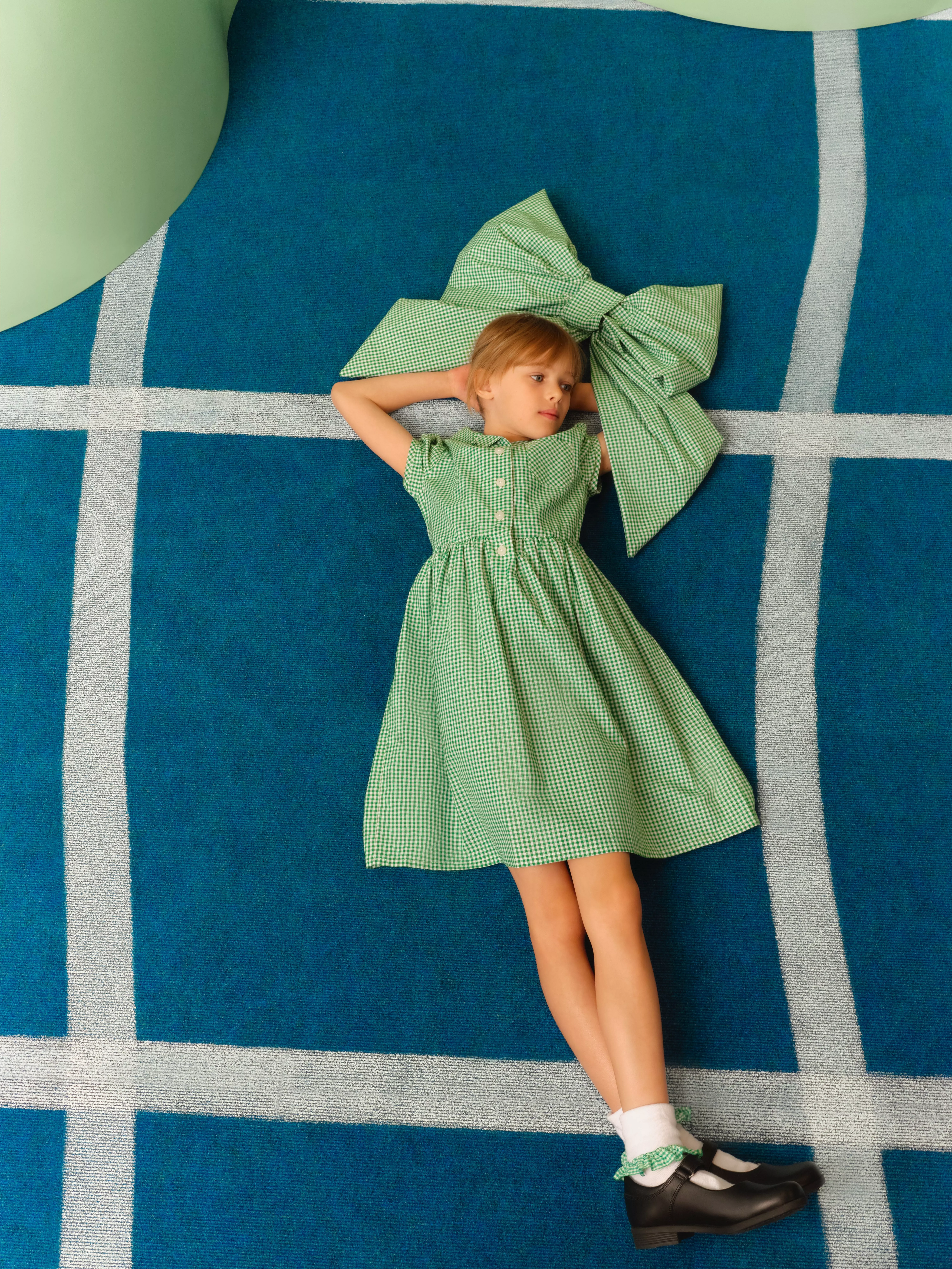 Two children in stylish outfits posing by a green wall with bold pink flower shapes, fashion photoshoot scene