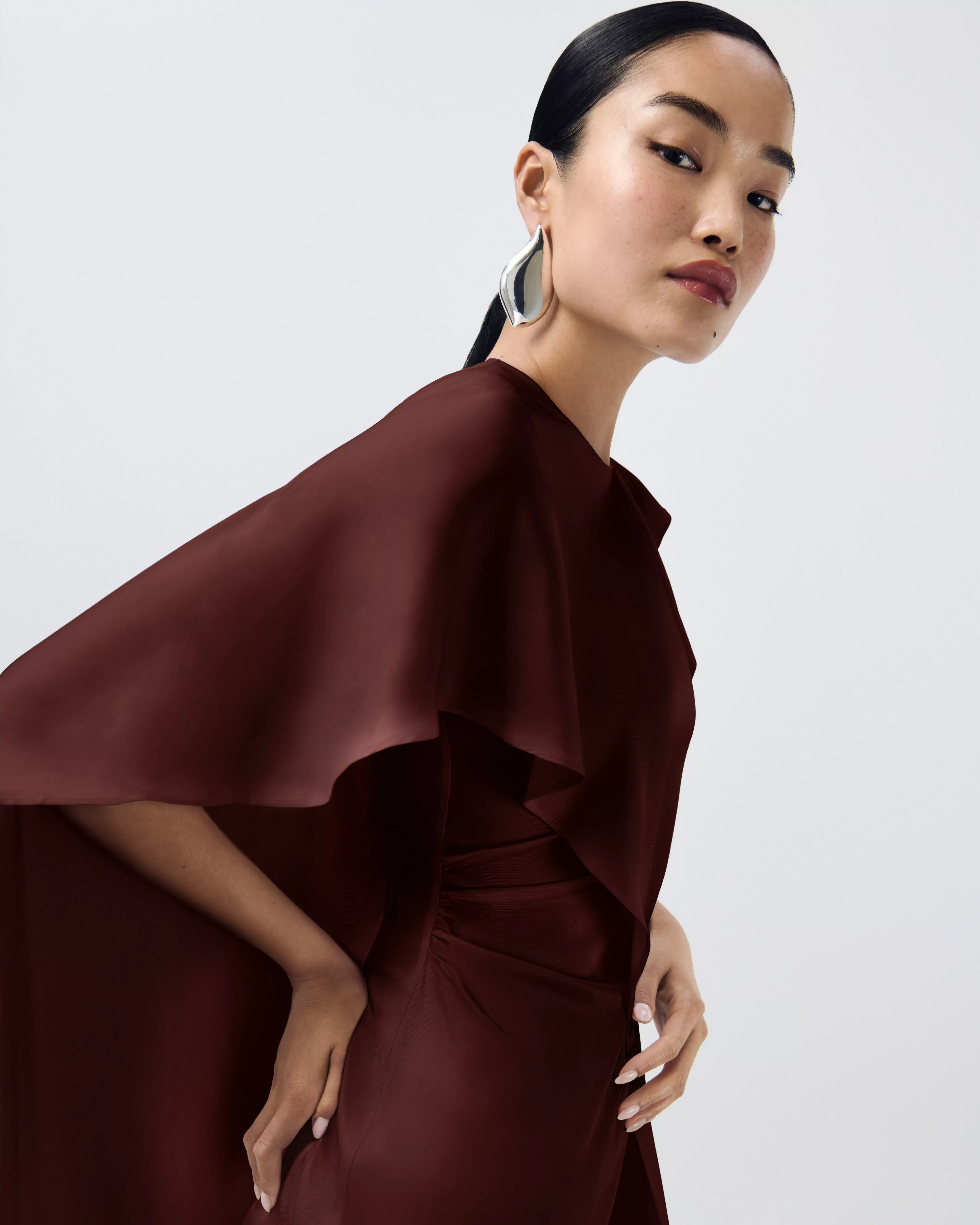 woman in burgundy cape satin dress with statement silver hoop earrings