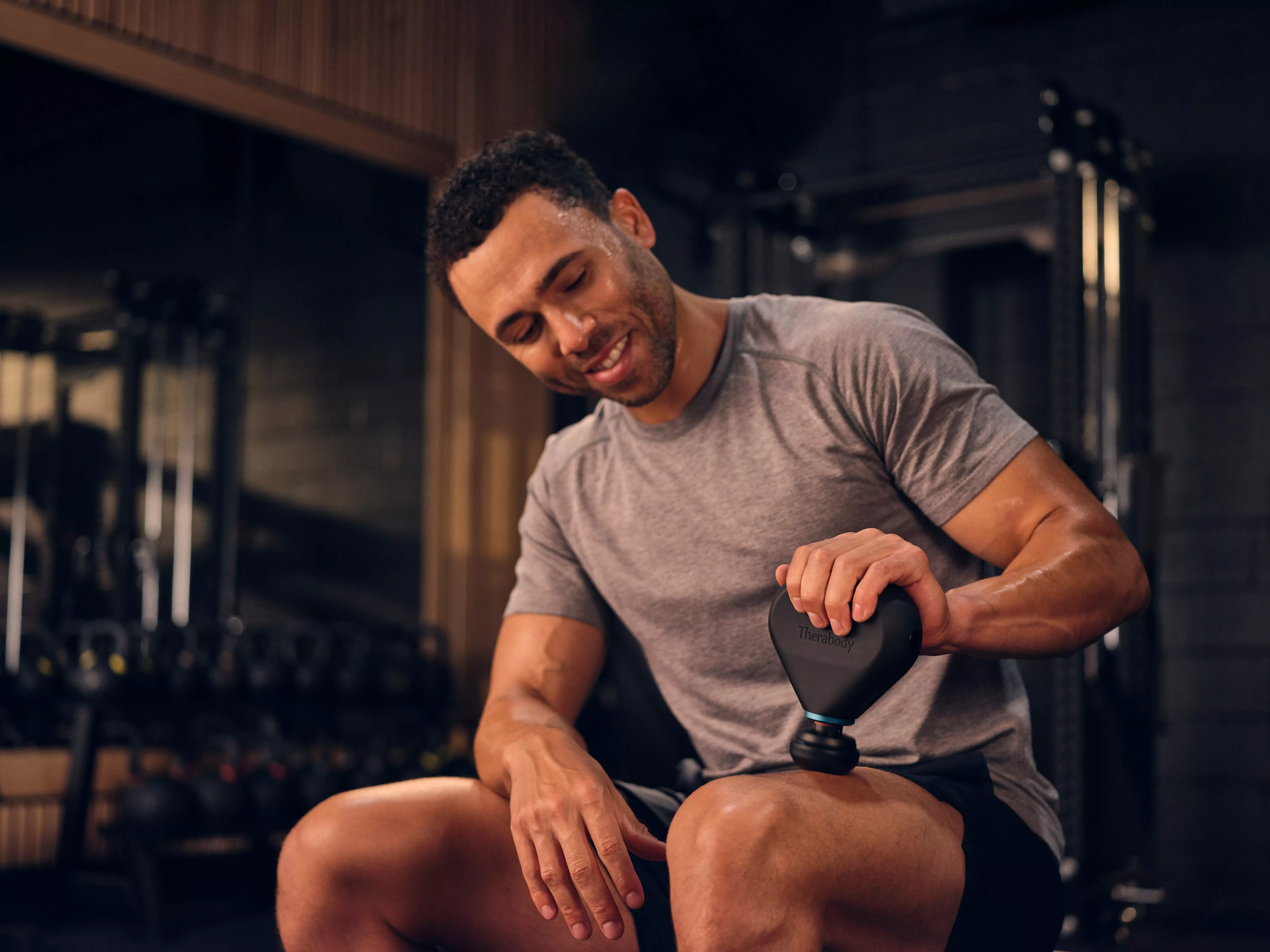 Man using Therabody massage gun on thigh in gym for muscle recovery after workout training session