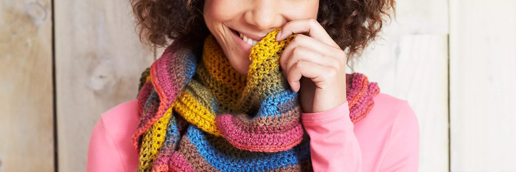 Smiling woman in pink top wearing a colourful hand-crocheted scarf, cosy winter fashion close-up