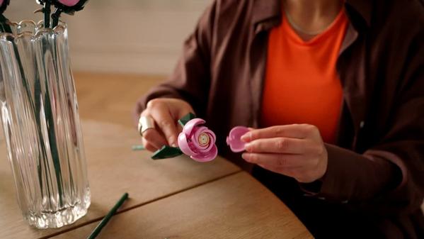 person's hands as they assemble a pink LEGO rose
