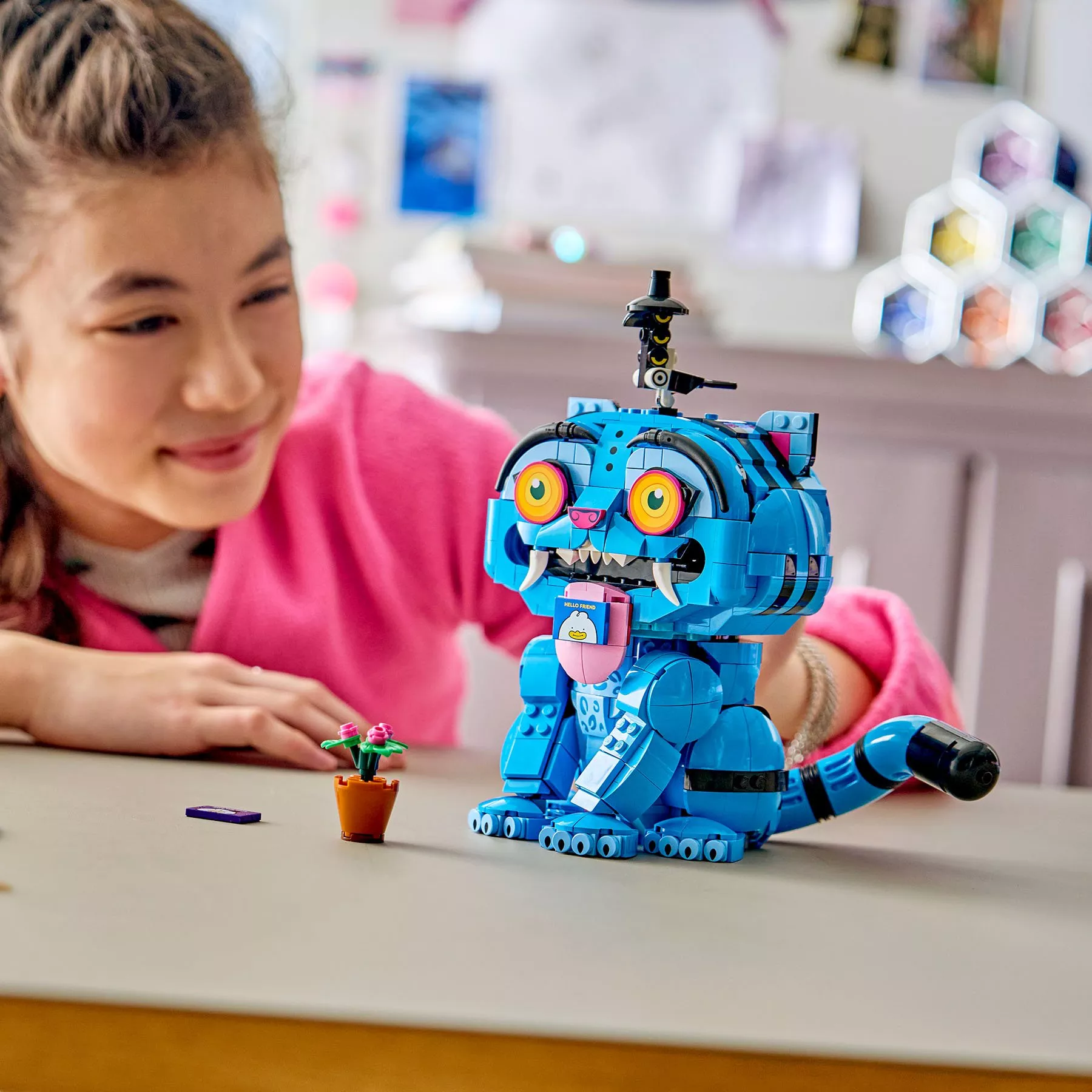 Child smiling beside a colourful blue LEGO cat model on a table, creative building toy for kids indoors