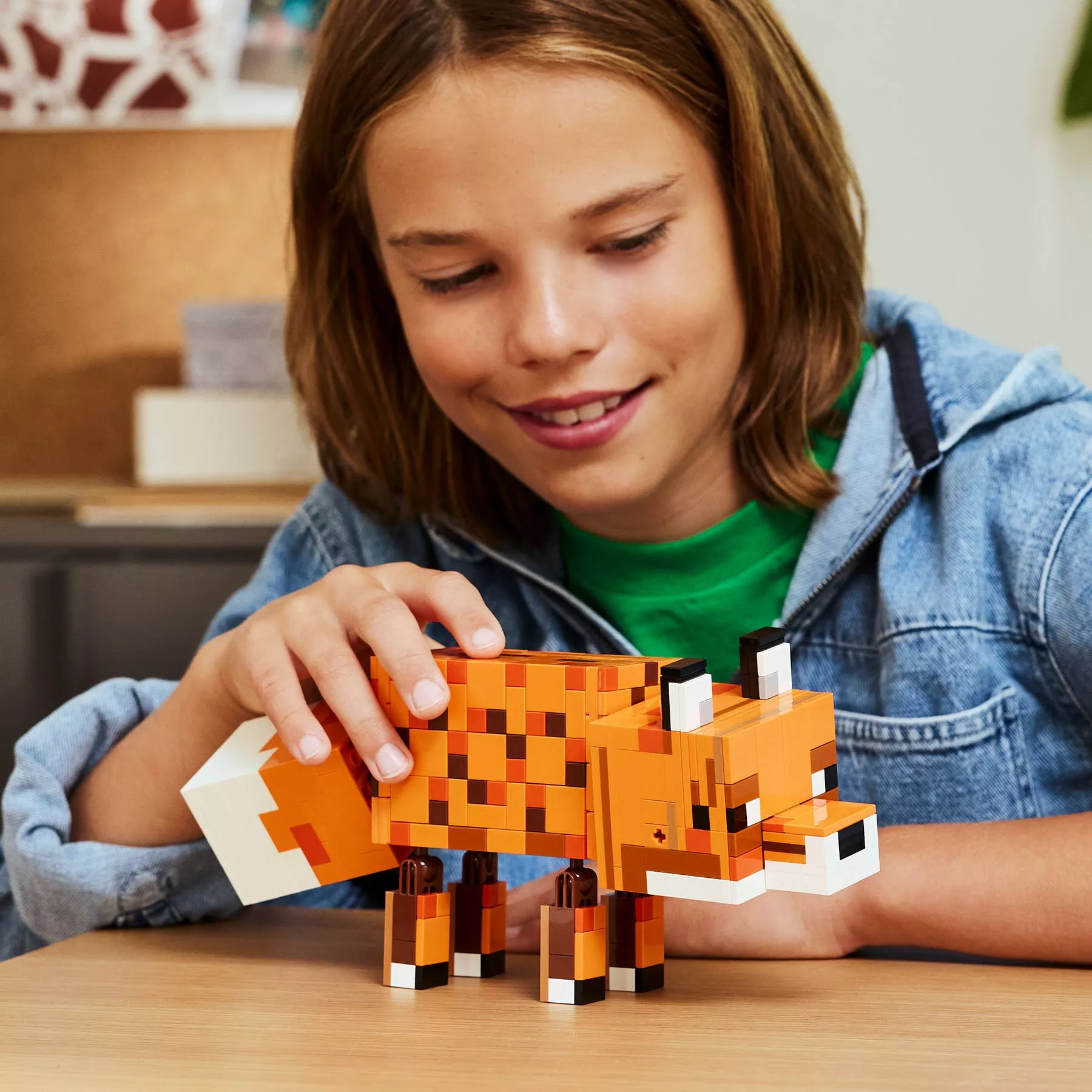 Smiling child playing with a brick-built orange fox toy model on a table, indoor creative building activity.