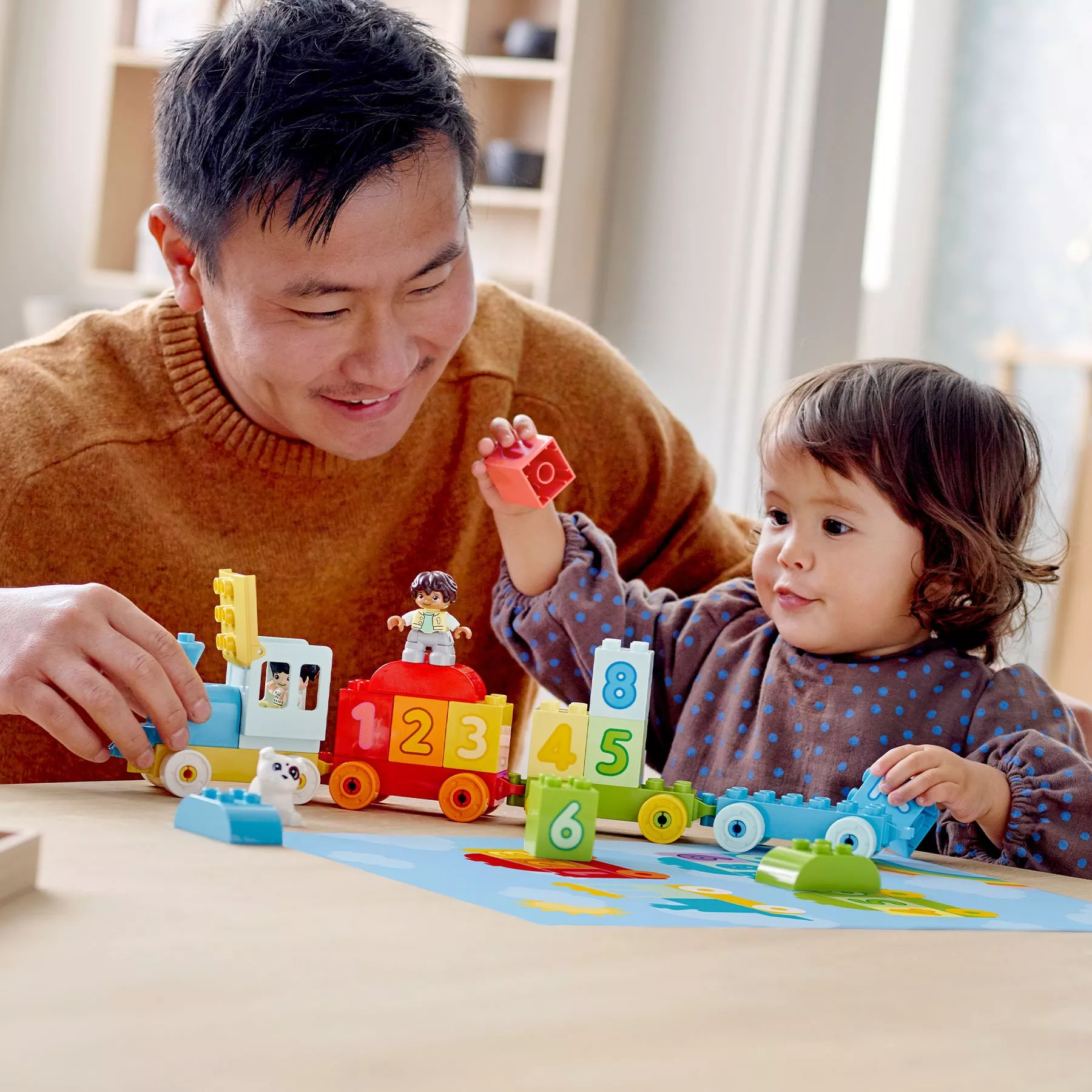 Father and toddler playing with colourful number train building blocks at home, learning through toy play together