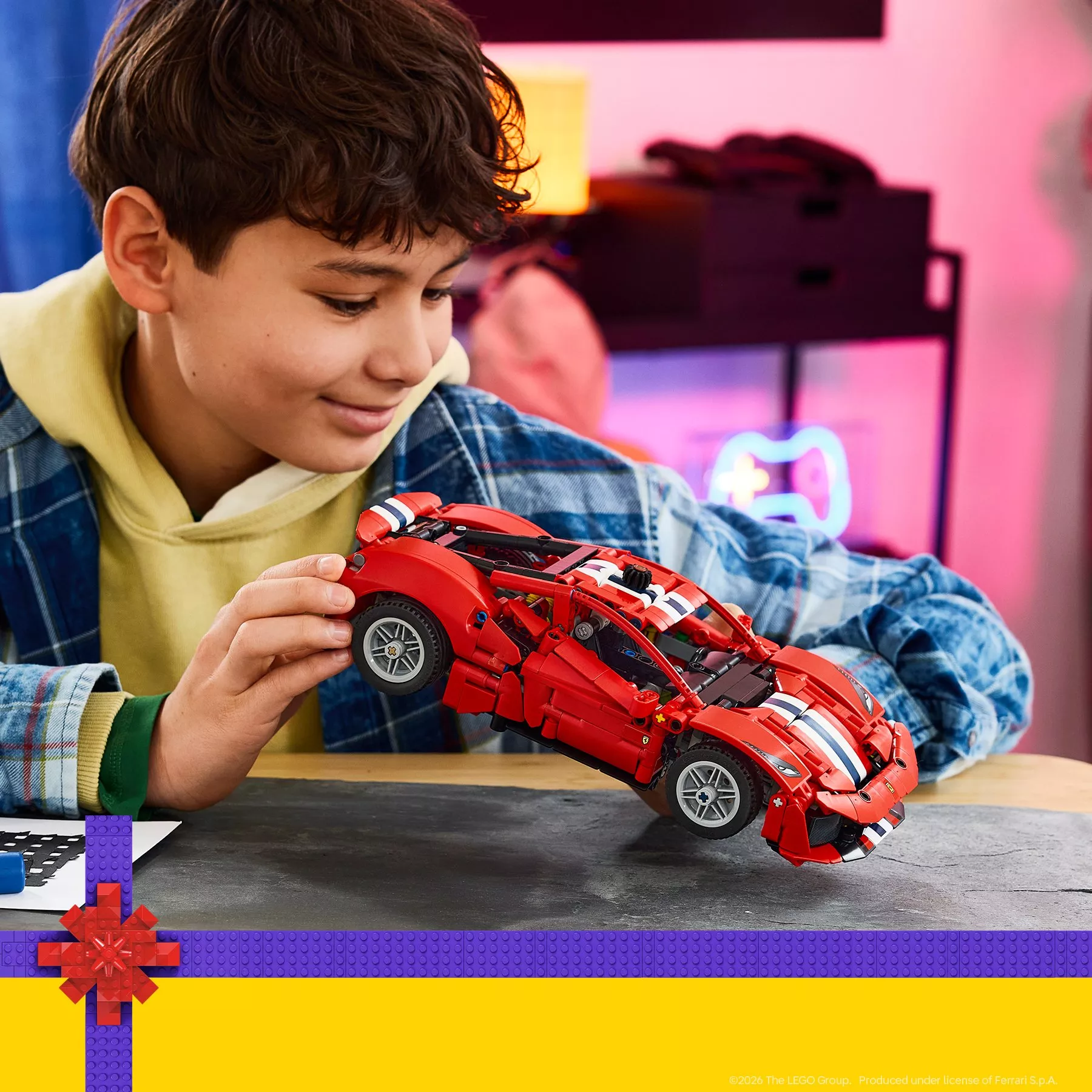 A boy smiling as he plays with a red LEGO Technic sports car model with blue and white racing stripes.