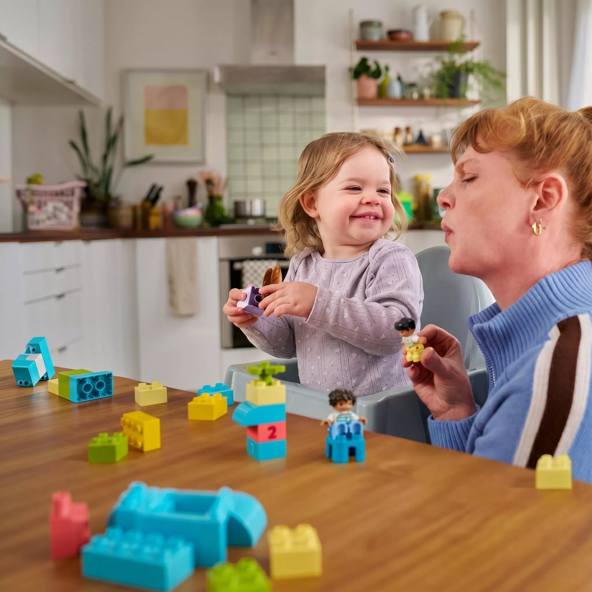 A mother and a child playing with LEGO Duplo building blocks on a table