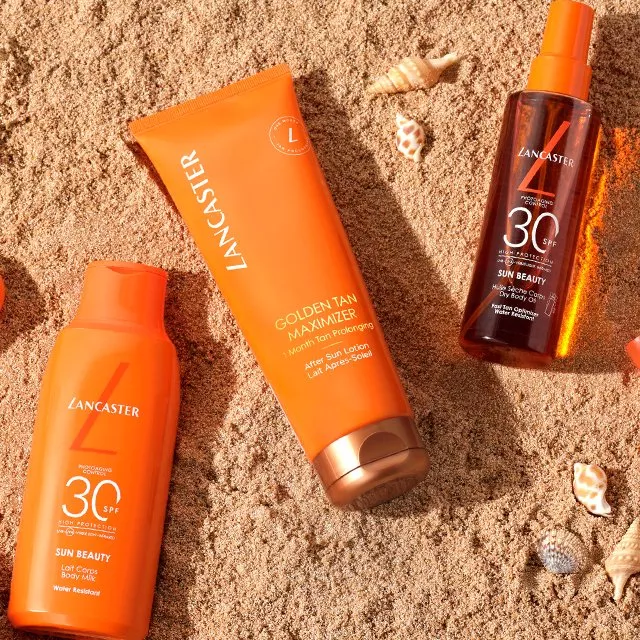 Lancaster sun care products on sandy beach, SPF 30 lotion and golden tan maximiser with seashells flat lay
