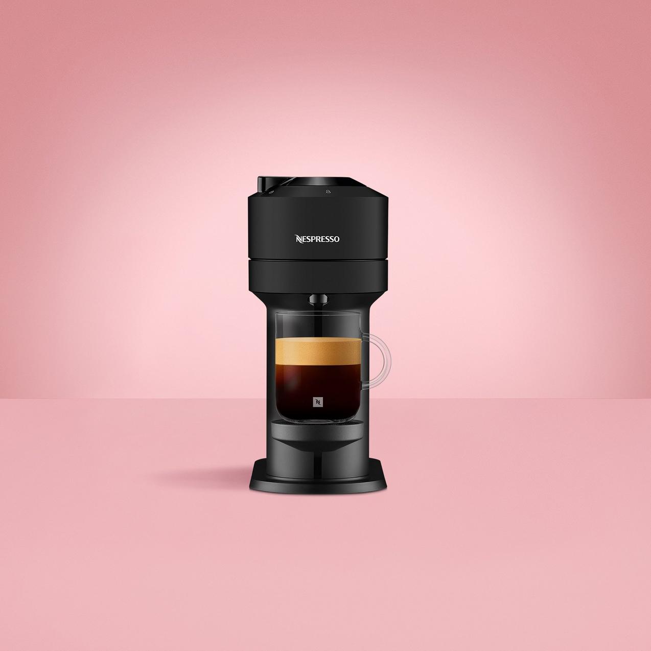 Nespresso Vertuo Pop machine with a fresh espresso, a silver travel mug, a glass of iced coffee, a milk frother, and a coffee pod on a solid blue background.