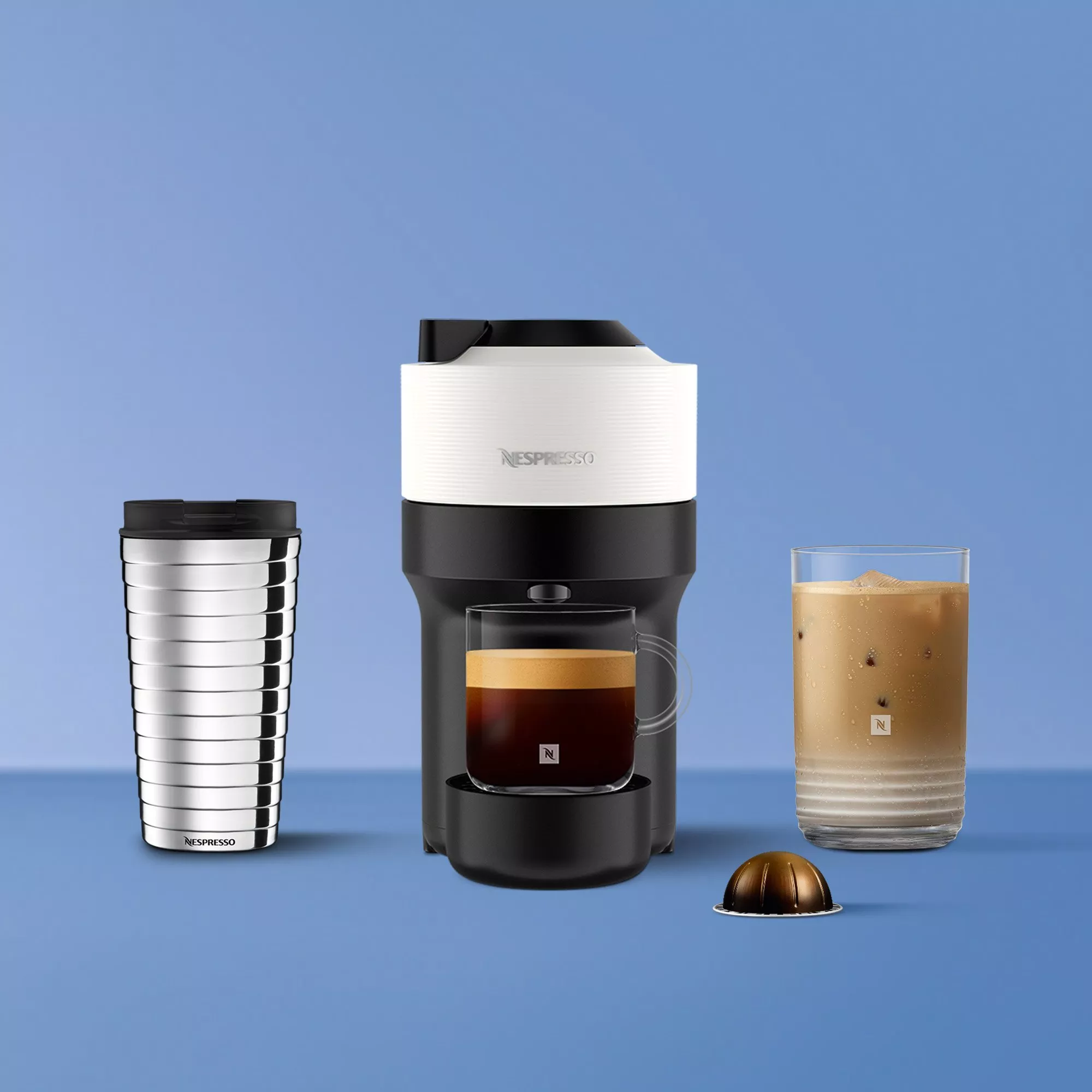 Nespresso Vertuo coffee machine with travel mug, espresso cup, iced latte glass and capsule on blue background