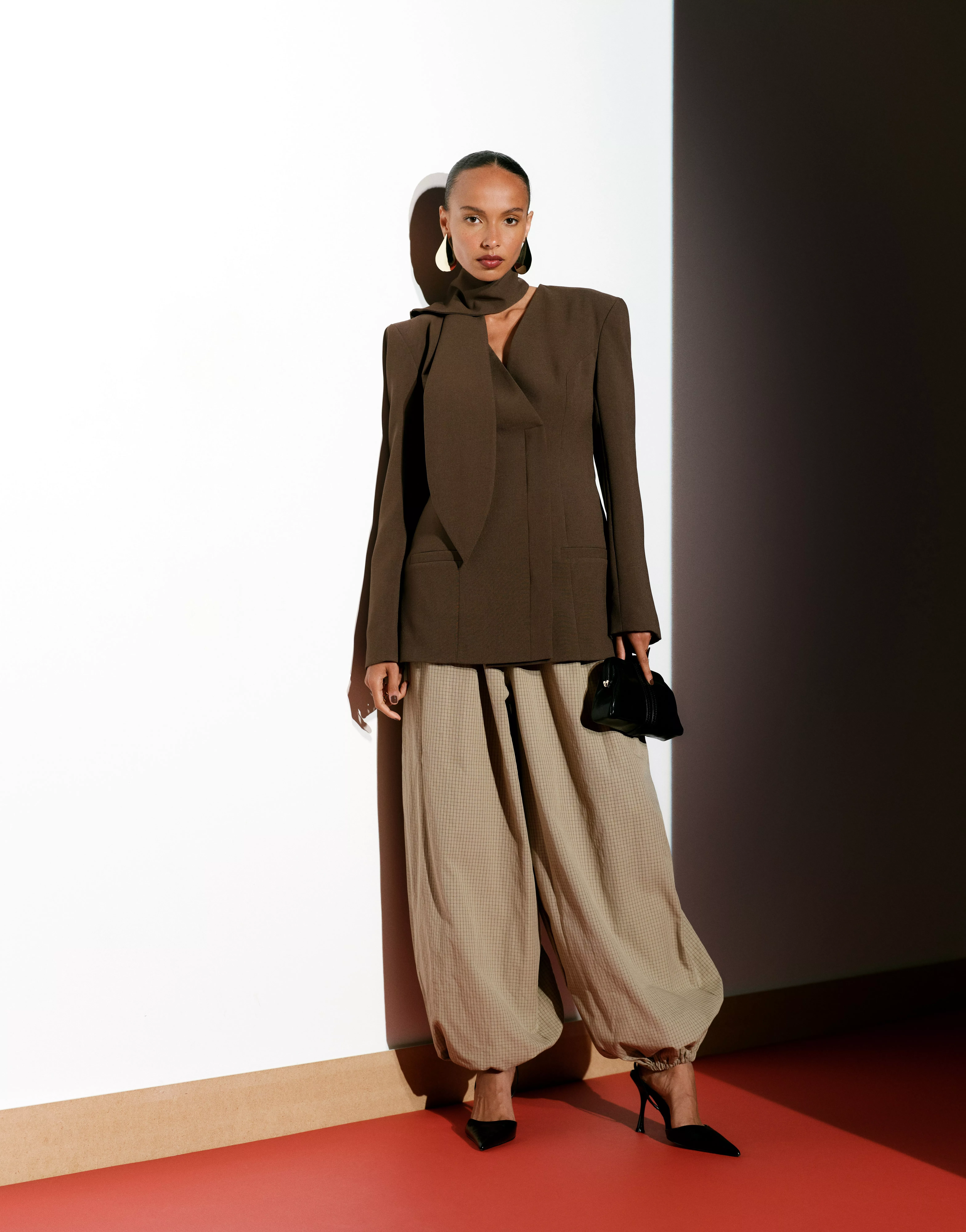 Fashion model in orange corridor wearing polka-dot blouse and wide-leg trousers, holding red leather handbag