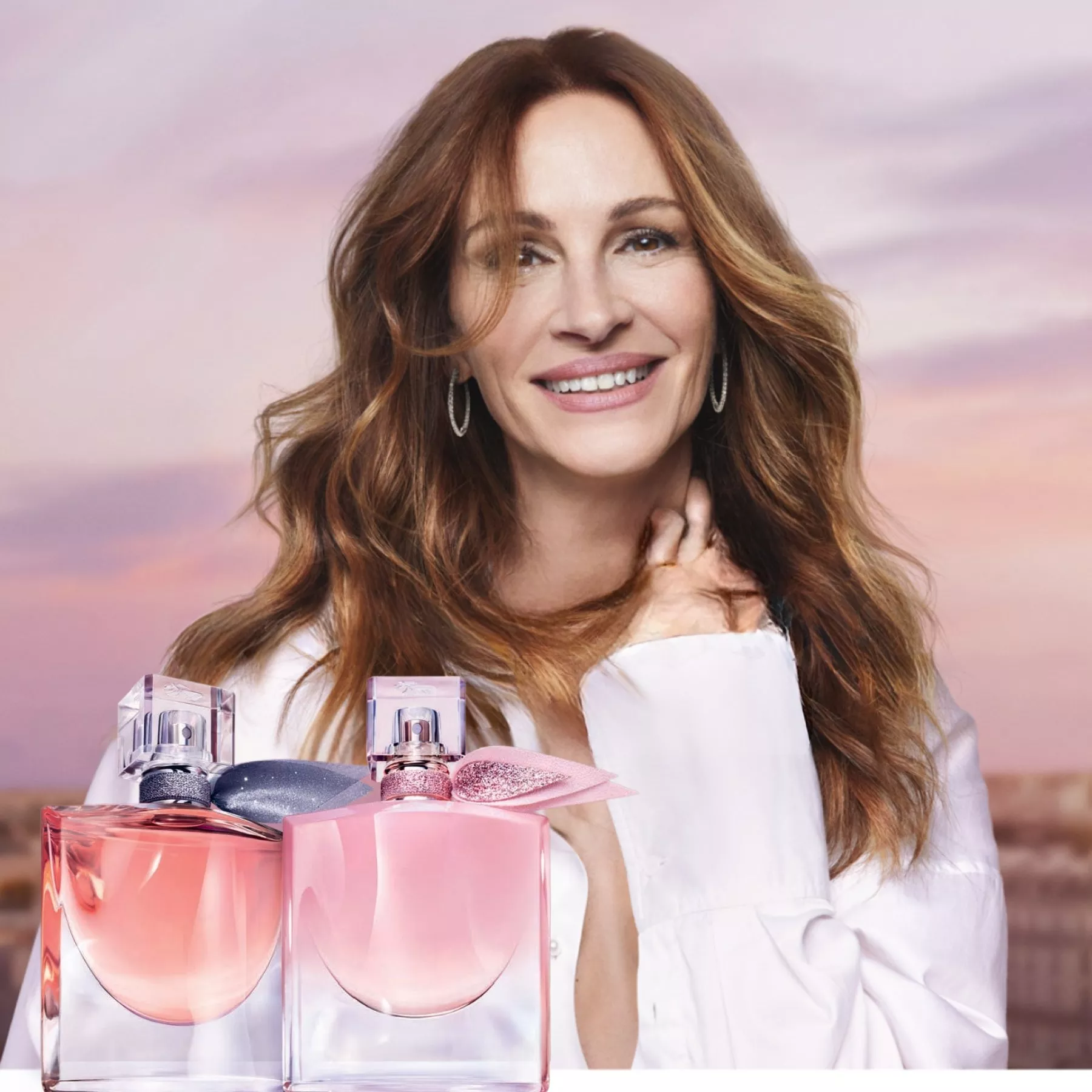 Woman smiling with long hair against a pastel sky, with two pink perfume bottles in the foreground.