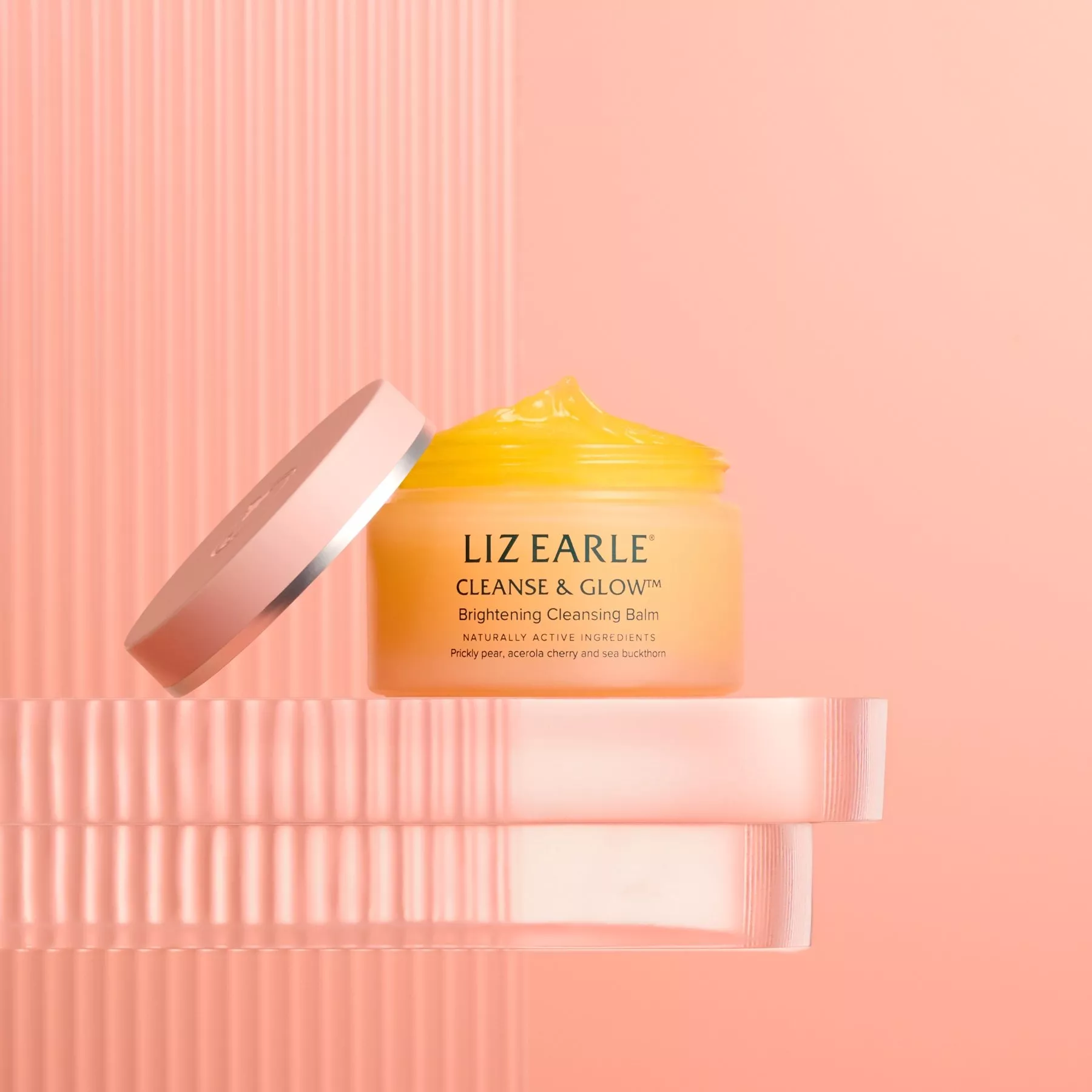 Liz Earle Cleanse & Glow brightening cleansing balm jar with lid off, yellow balm on pink studio background