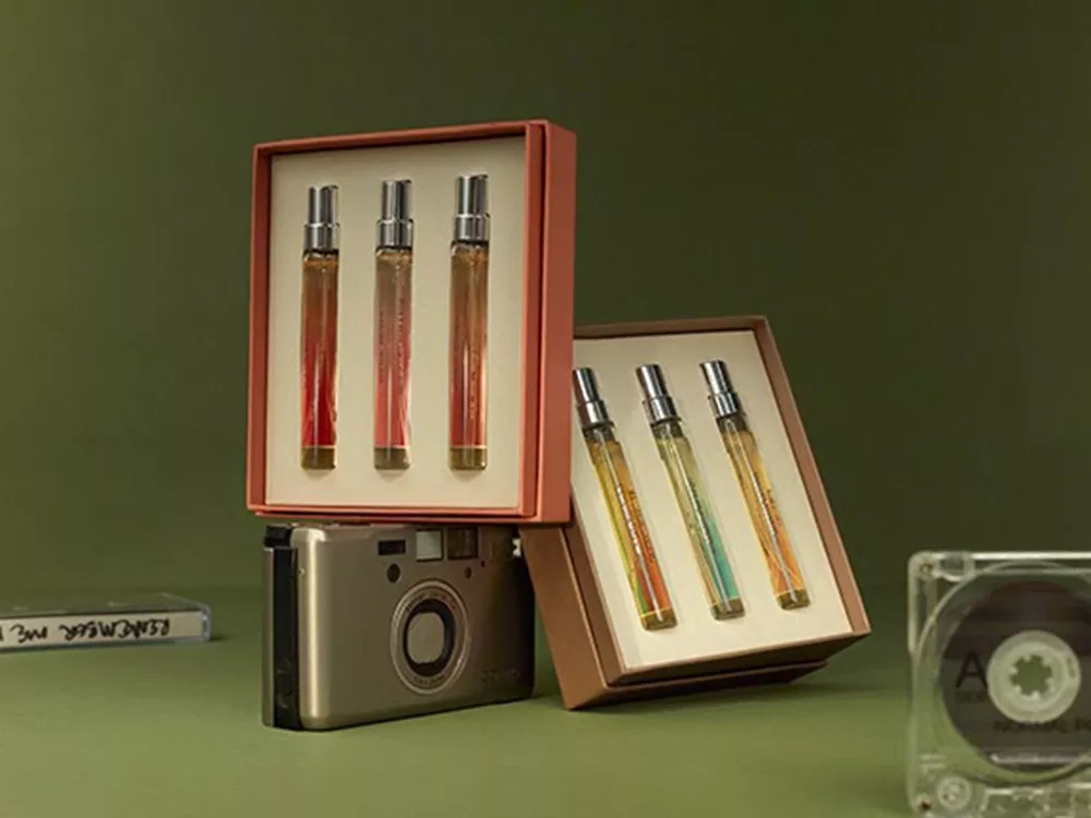 Perfume sets in open boxes, displayed with a vintage camera and cassette tapes on a green background.