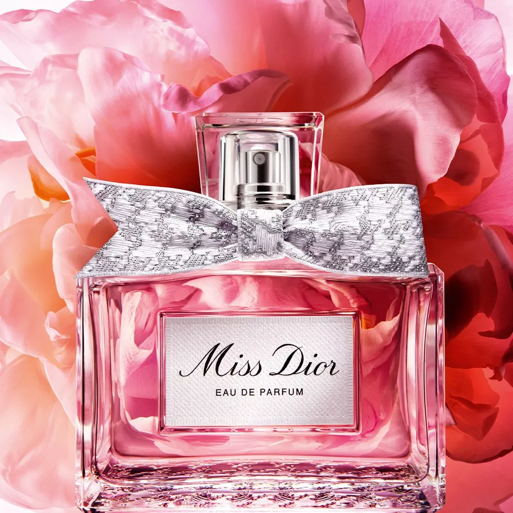 Miss Dior Eau de Parfum bottle with silver bow, pink glass and rose petals background, luxury fragrance close-up