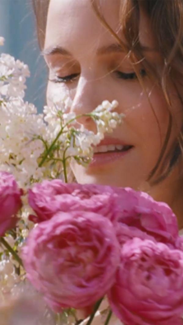 Close-up of woman smelling pink roses and white blossoms, soft natural light, romantic floral portrait outdoors