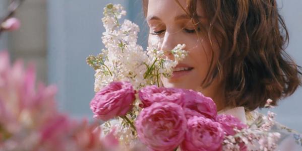 Close-up of woman smelling bouquet of pink roses and white blossoms in soft sunlight, romantic spring flowers
