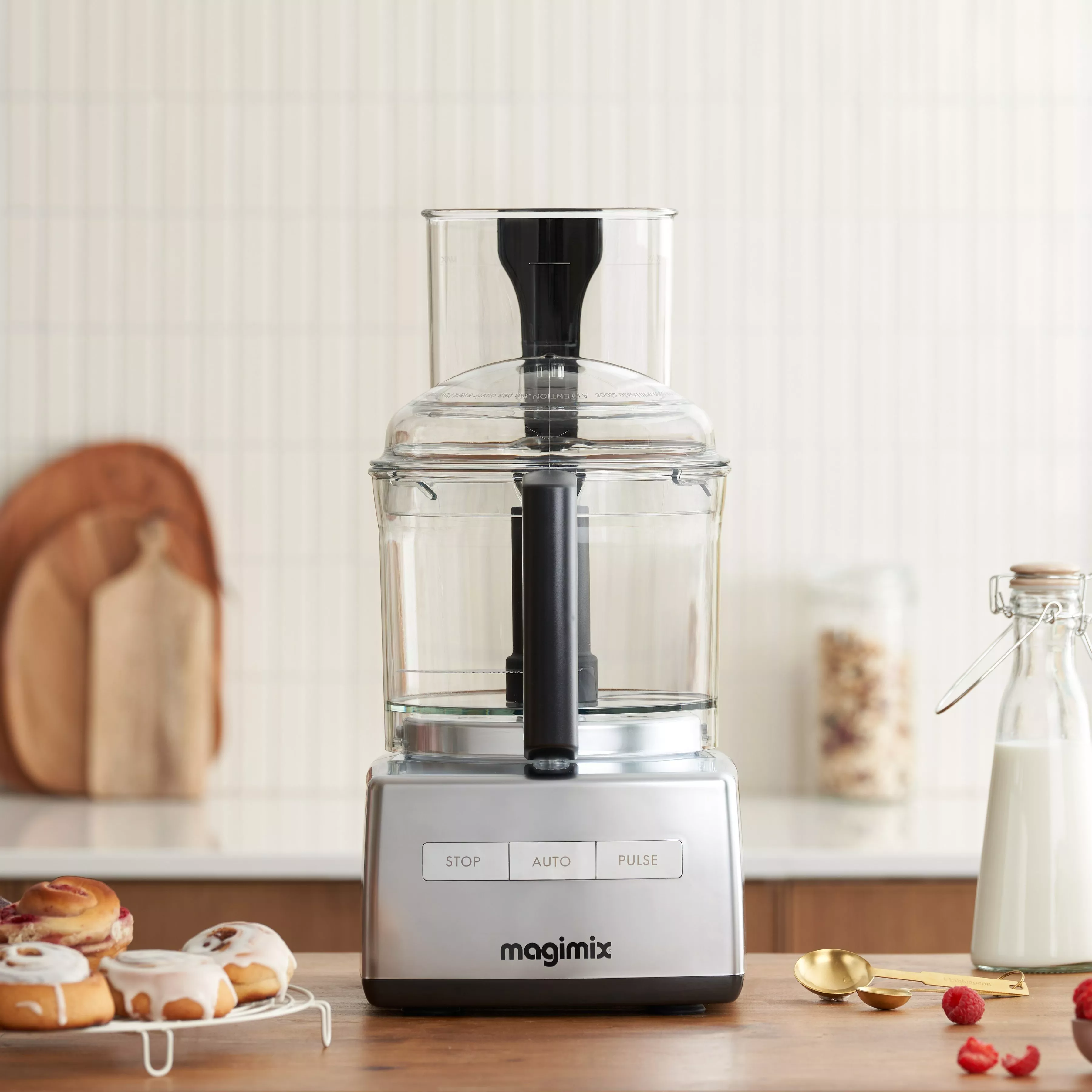 Magimix food processor on kitchen worktop with pastries, milk bottle and measuring spoons, modern home setting.