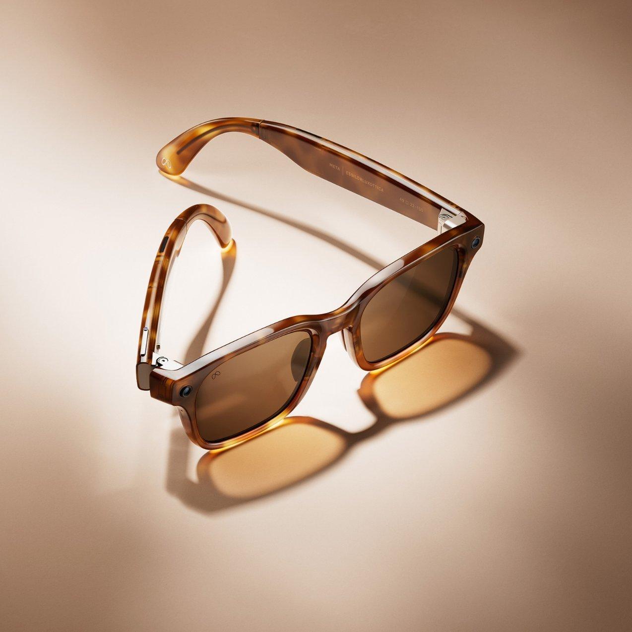 A top-down shot of Ray-Ban Meta smart glasses in a shiny tortoiseshell frame with brown lenses, resting on a beige surface with a soft shadow.