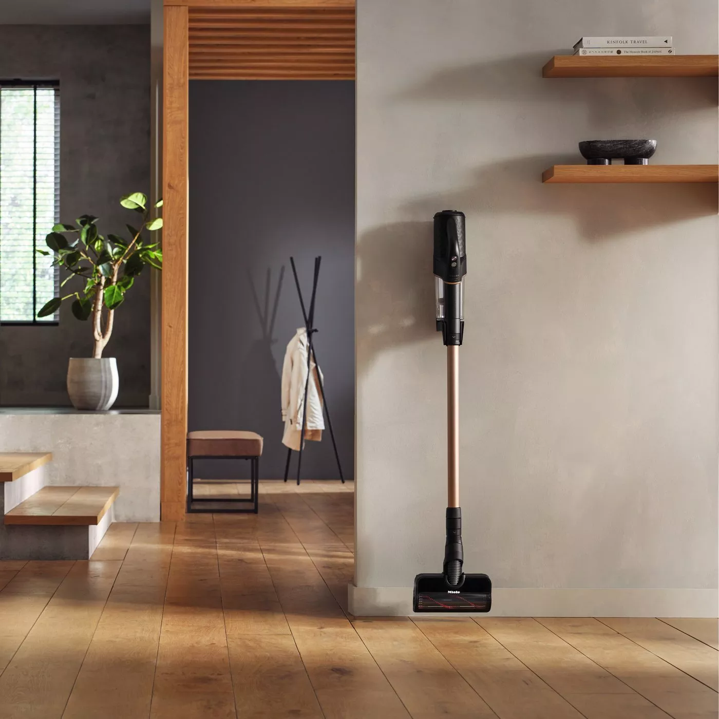 A modern, minimalist room with a sleek cordless vacuum cleaner resting against a wall, wooden floors, and decor.