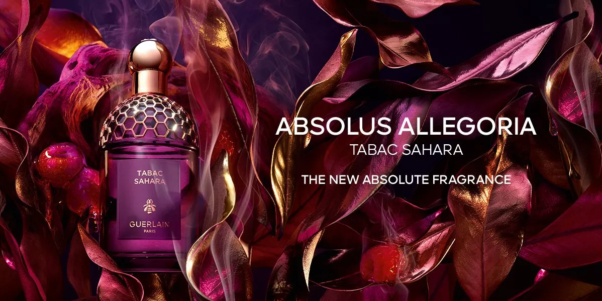 A Guerlain Absolus Allegoria "Tabac Sahara" perfume bottle sits amidst shimmering, dark magenta and gold leaves. Smoke curls around the bottle, with the text "The New Absolute Fragrance."