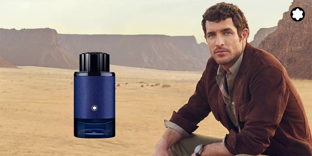 Montblanc cologne banner featuring a blue fragrance bottle on the left and a man in a jacket on the right, set against a desert landscape with cliffs.