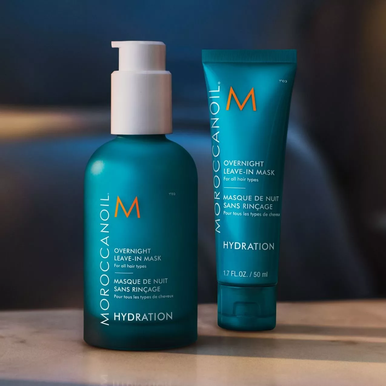 Moroccanoil Overnight Leave-In Mask bottle with pump dispenser next to a smaller squeeze tube on a wooden surface.