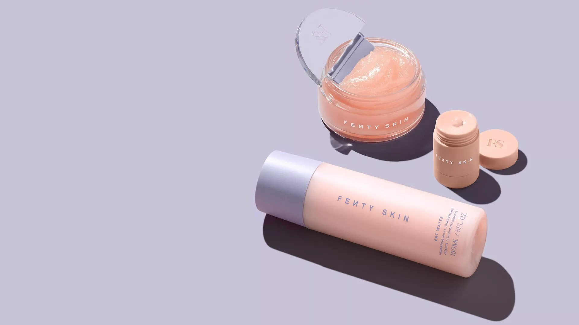 Fenty Skin products on a pastel surface, featuring a bottle, jar, and stick, showcasing skincare essentials.