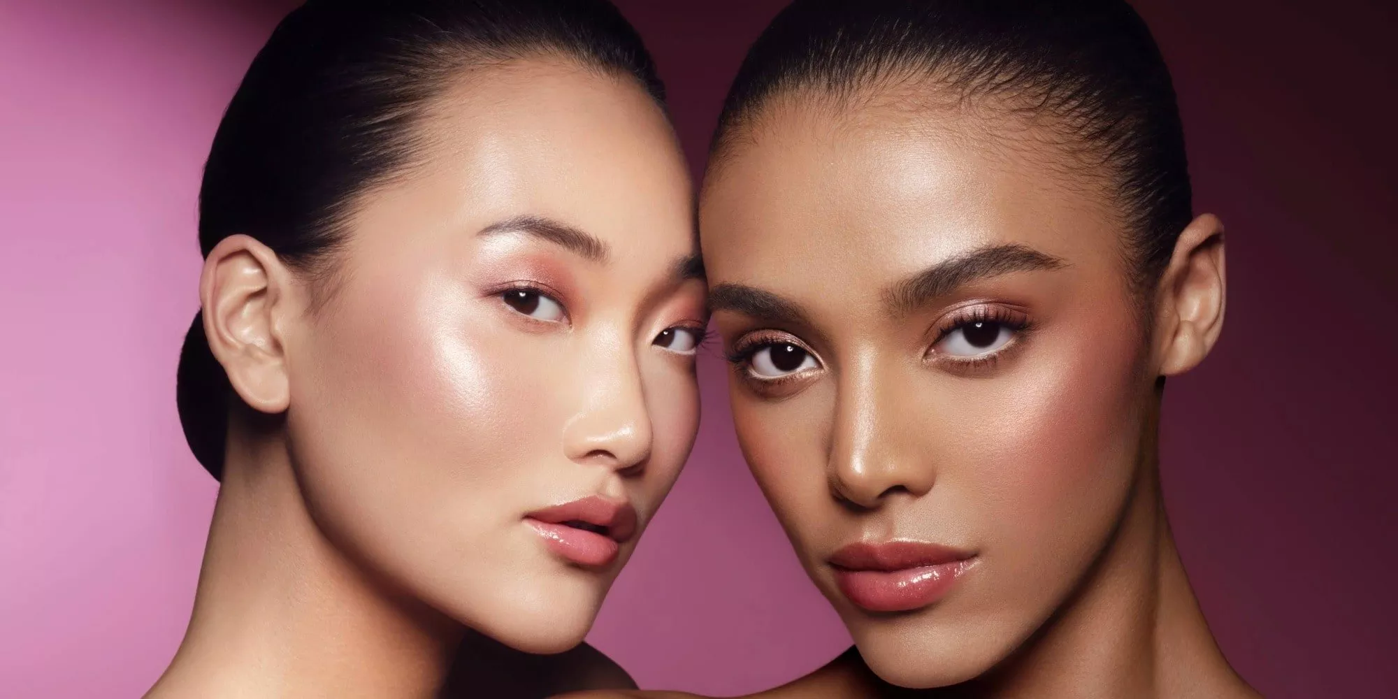 Two models with glowing skin, dewy highlight and soft pink eyeshadow, showcasing natural beauty makeup on pink backdrop