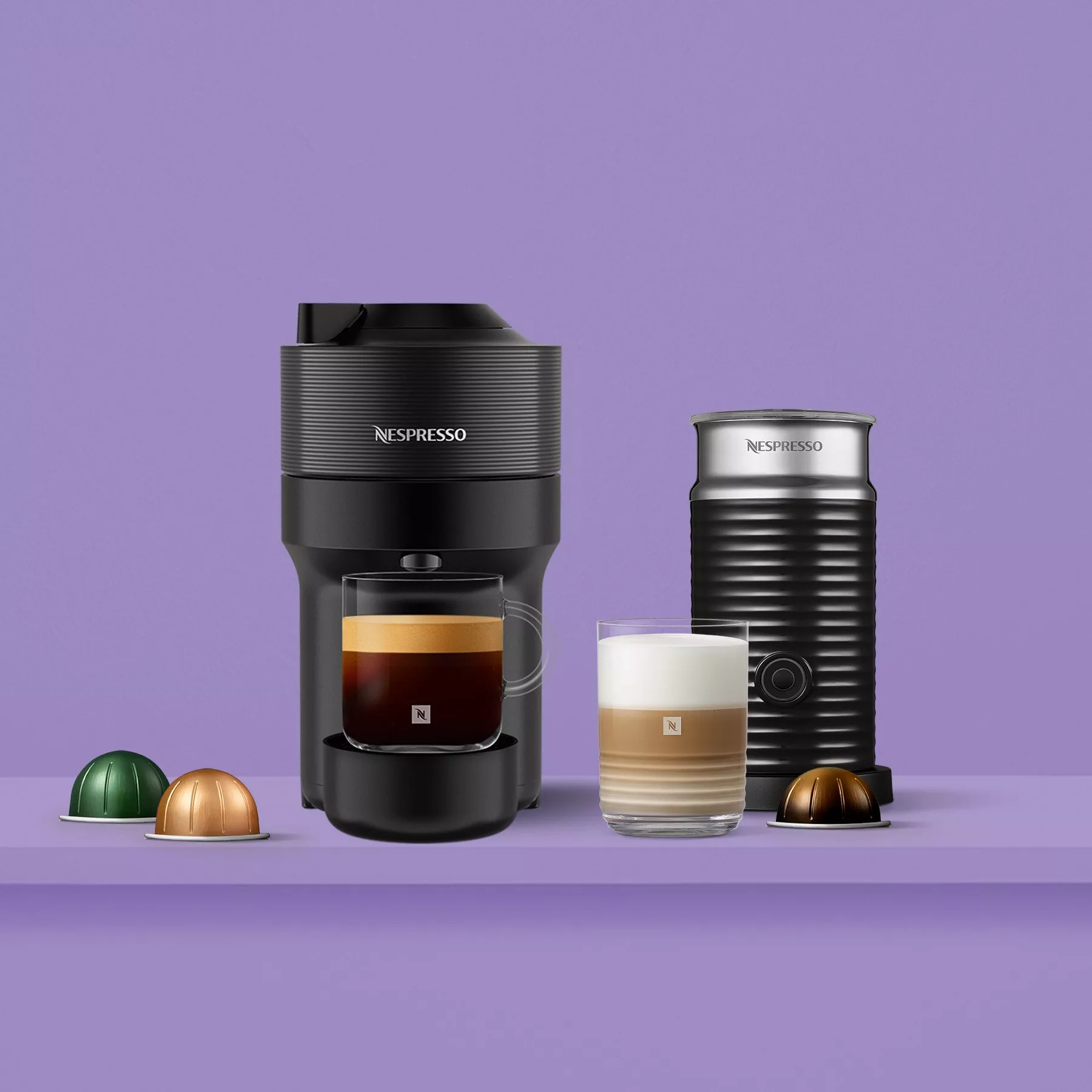 Nespresso coffee machine and frother on a purple background, with coffee pods and espresso cups displayed.
