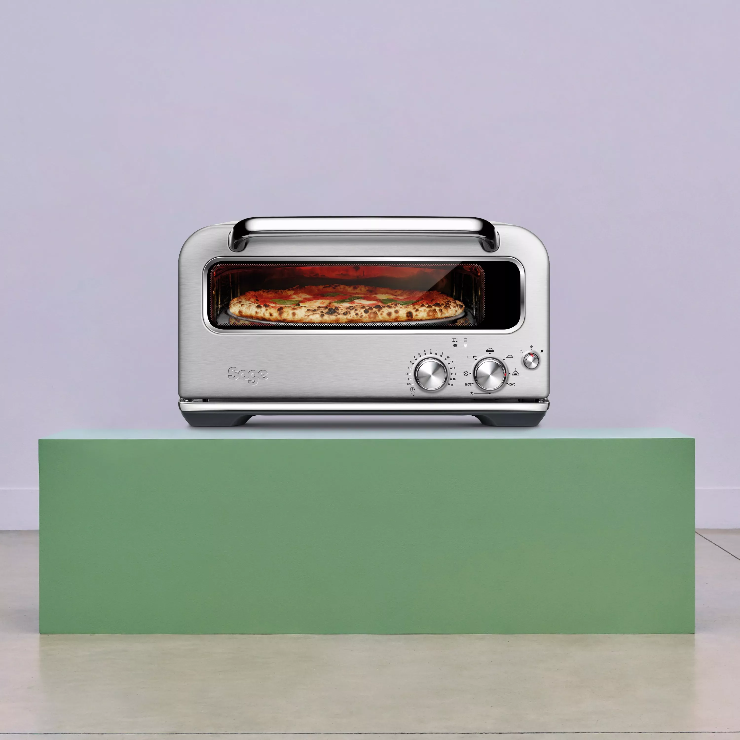 Stainless steel countertop pizza oven baking a fresh pizza, with temperature dials and viewing window on display