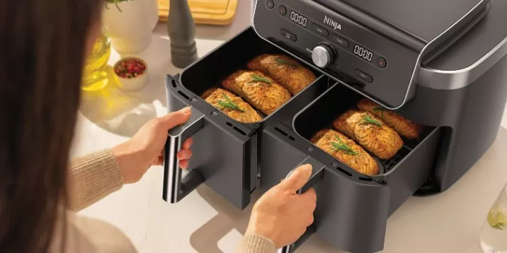 Ninja dual drawer air fryer with salmon fillets cooking, hands pulling baskets out on kitchen worktop