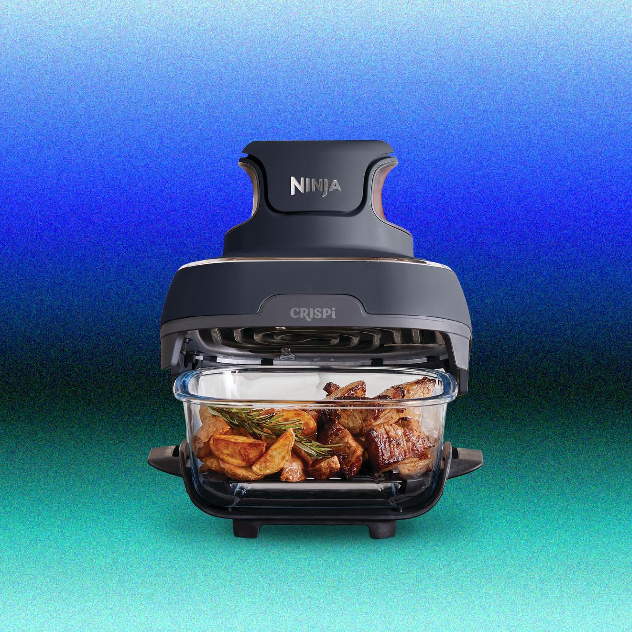 A dark gray Ninja Crispi portable air fryer module seated atop a clear glass container filled with cooked chicken wings, next to a smaller glass container with cooked salmon and broccoli.