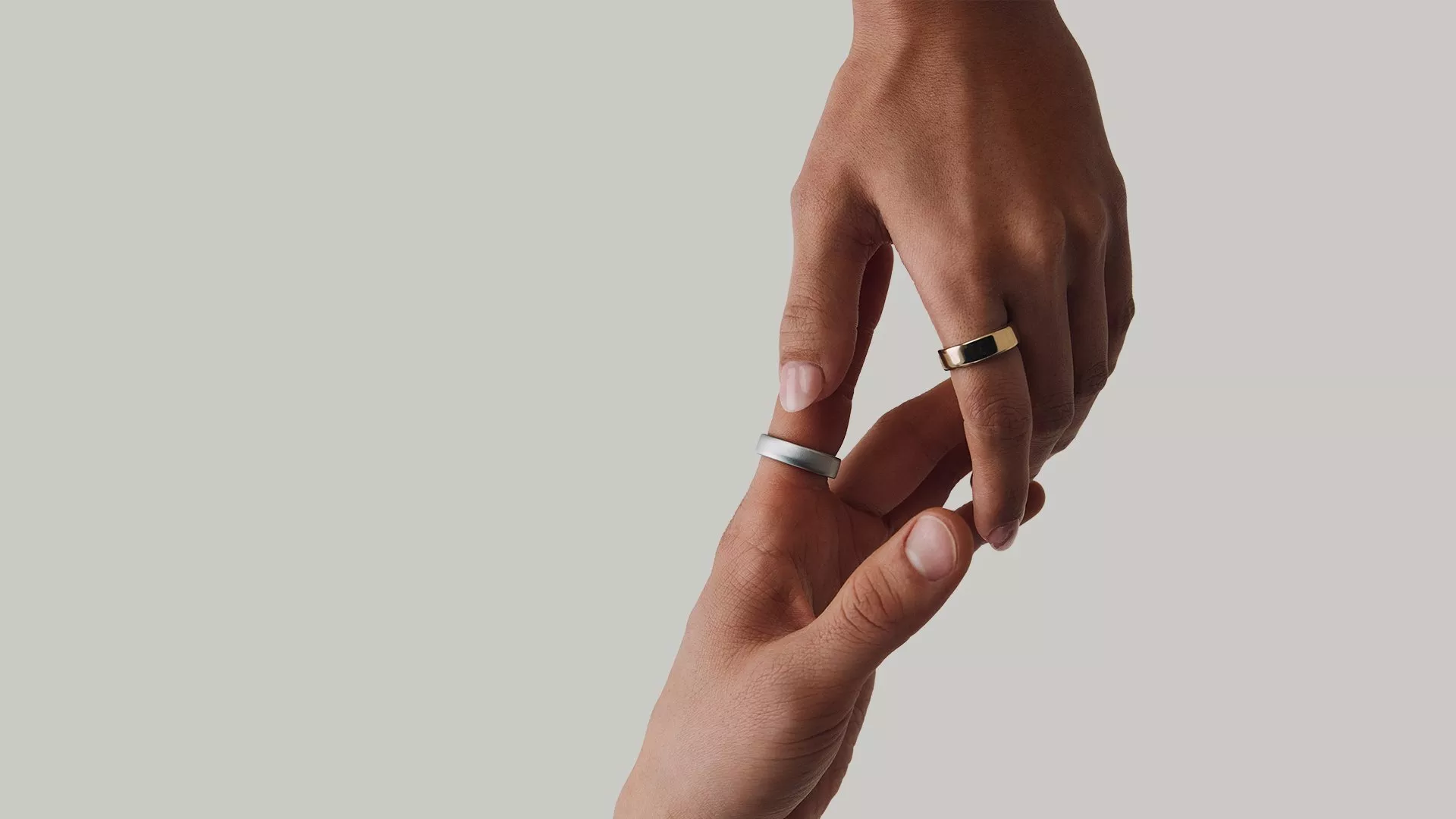 Close-up of hands wearing gold and silver wedding bands, gently touching against a neutral background