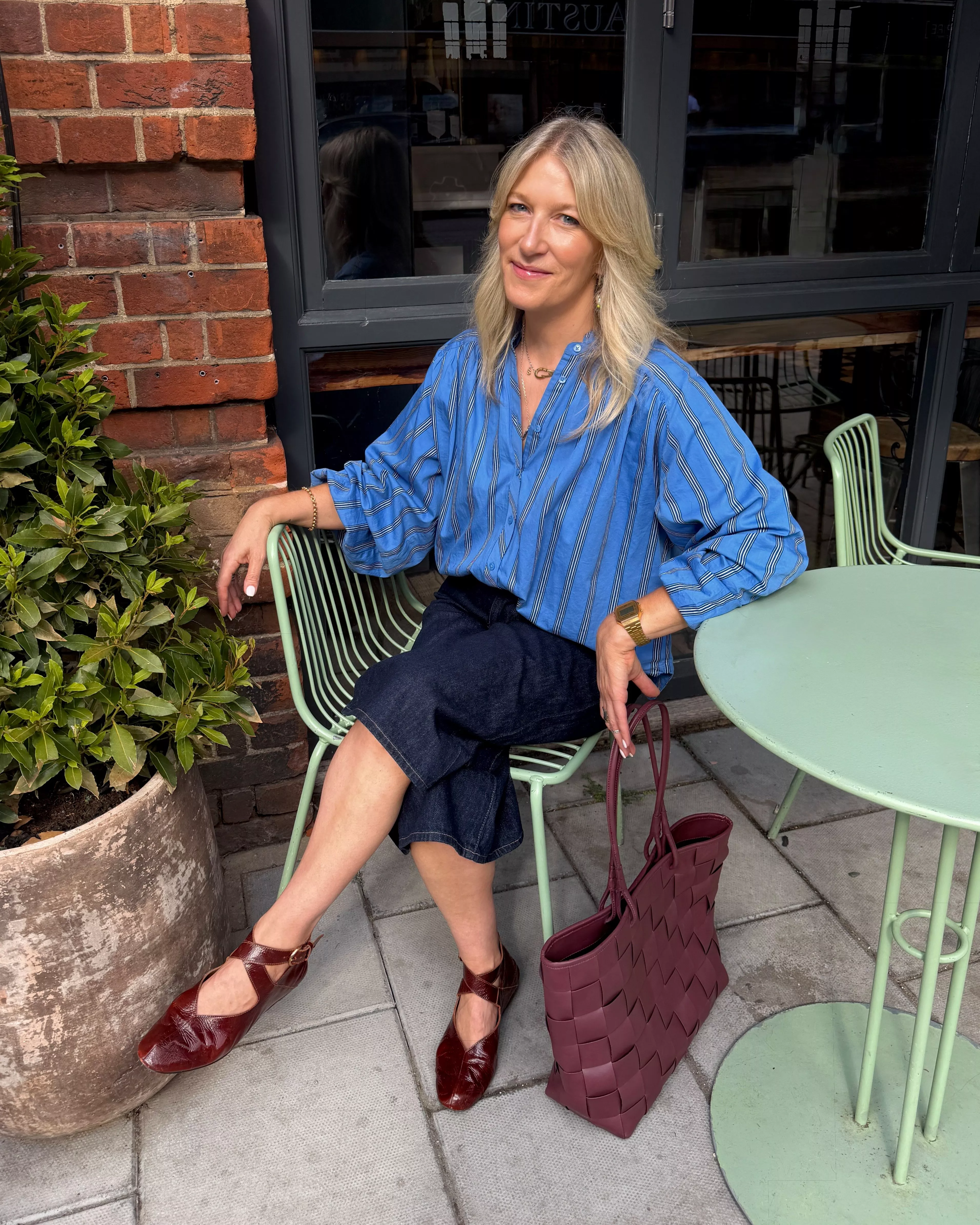 Stylist wearing a blue striped shirt with blue culottes, burgundy shoe and a burgundy bag