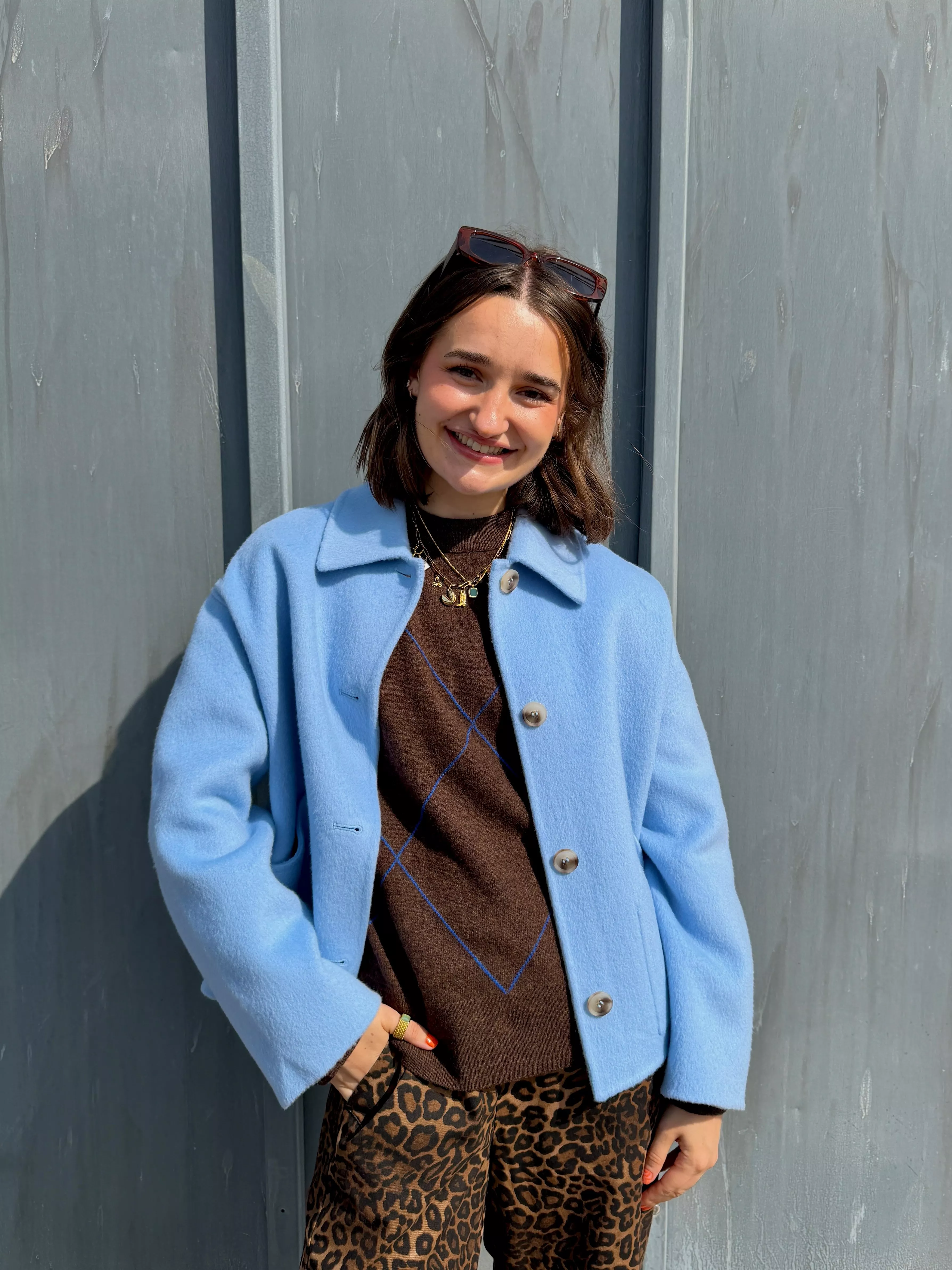 Stylist wearing a blue jacket, argyle jumper, leopard print trousers and sunglasses