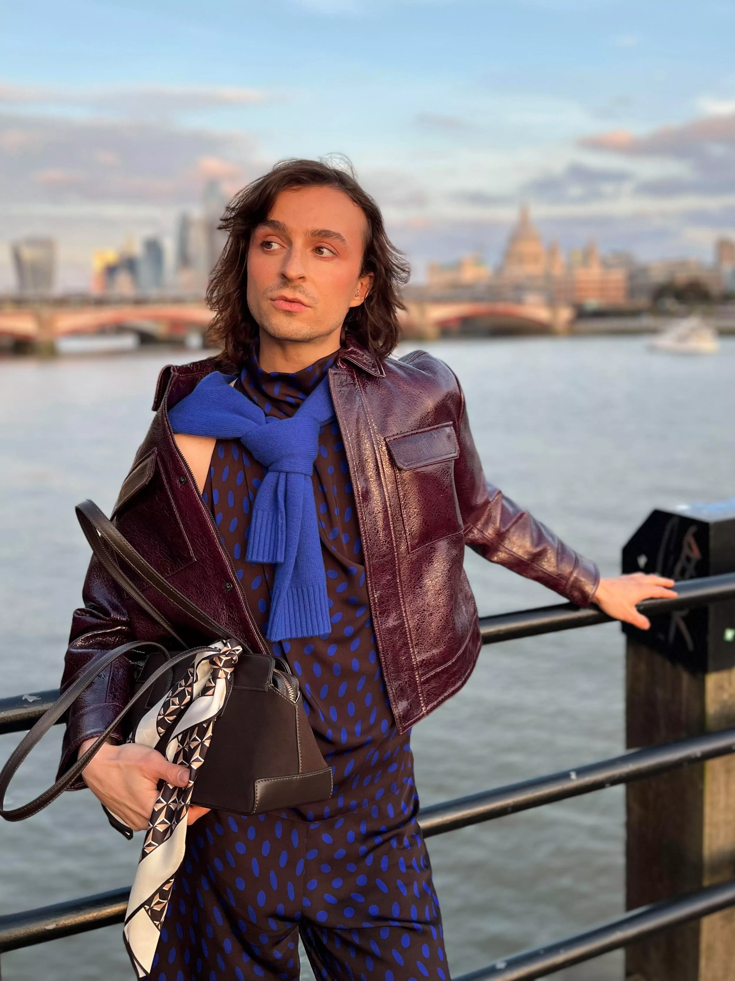 Stylist wearing a burgundy leather jacket, with blue jumper and bag