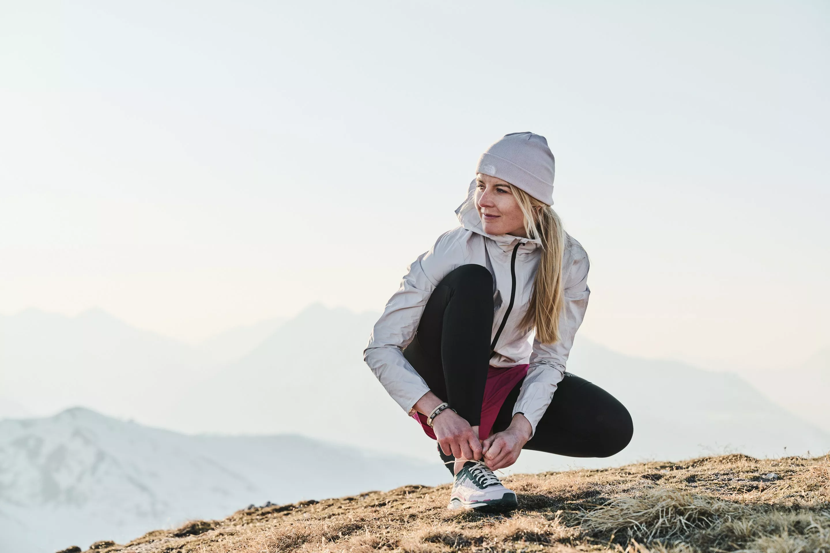 woman crouched down tying up her shoelace wearing outdoor workout clothing