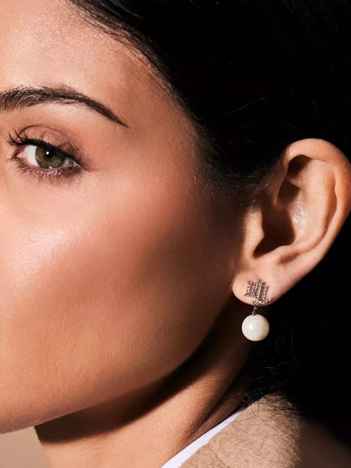 Close-up of woman wearing pearl drop earrings with crystal initials.