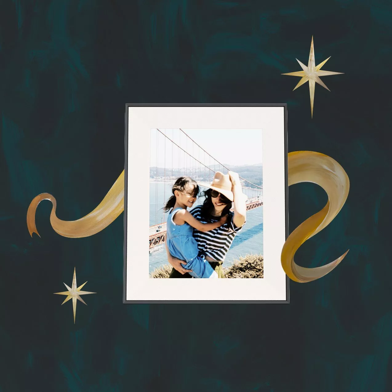 A framed photo of a woman holding a smiling child outdoors near the Golden Gate Bridge, set against a dark teal background with gold star and swirl accents.