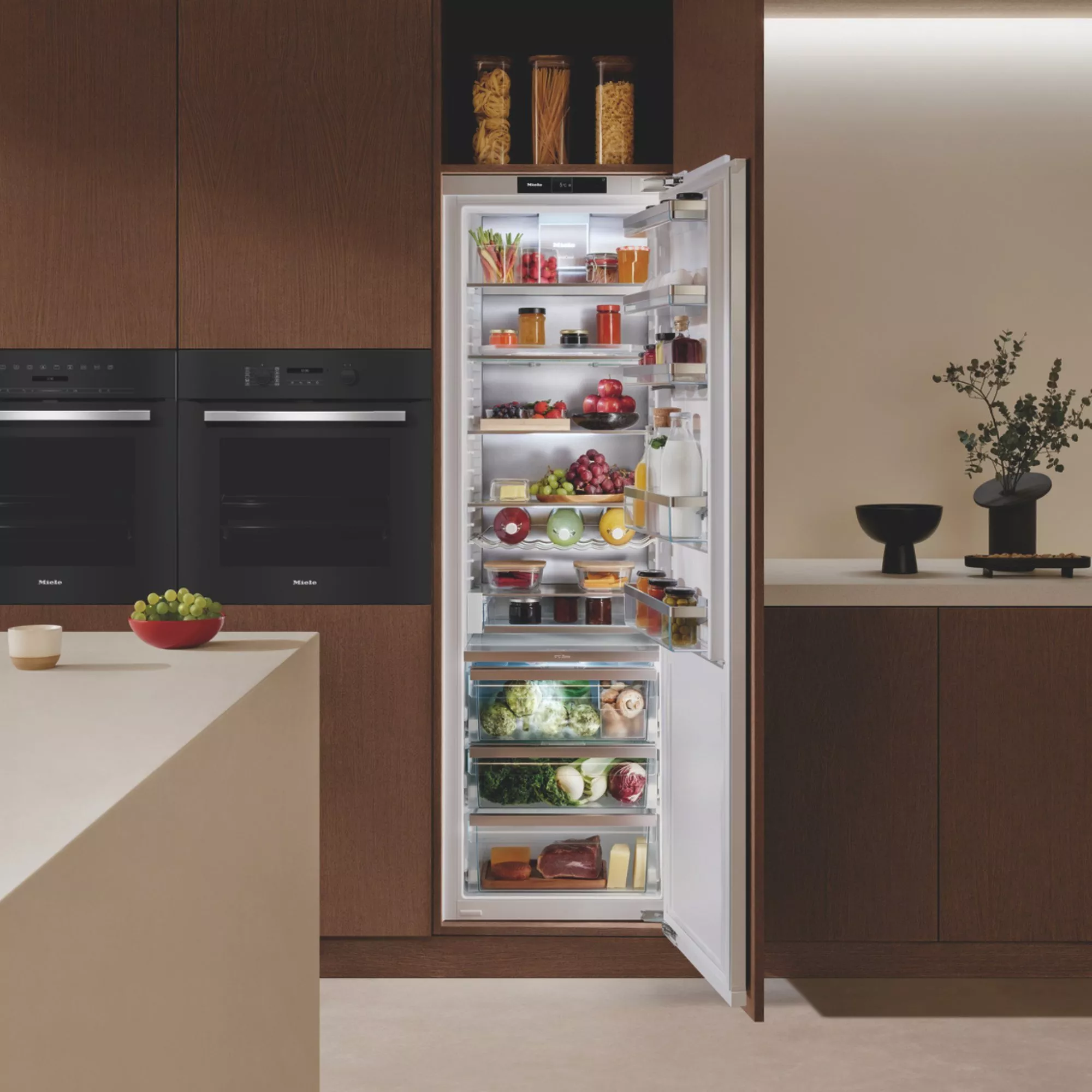Modern built-in Miele fridge in luxury kitchen, door open showing organised fresh food, fruit, vegetables and drinks